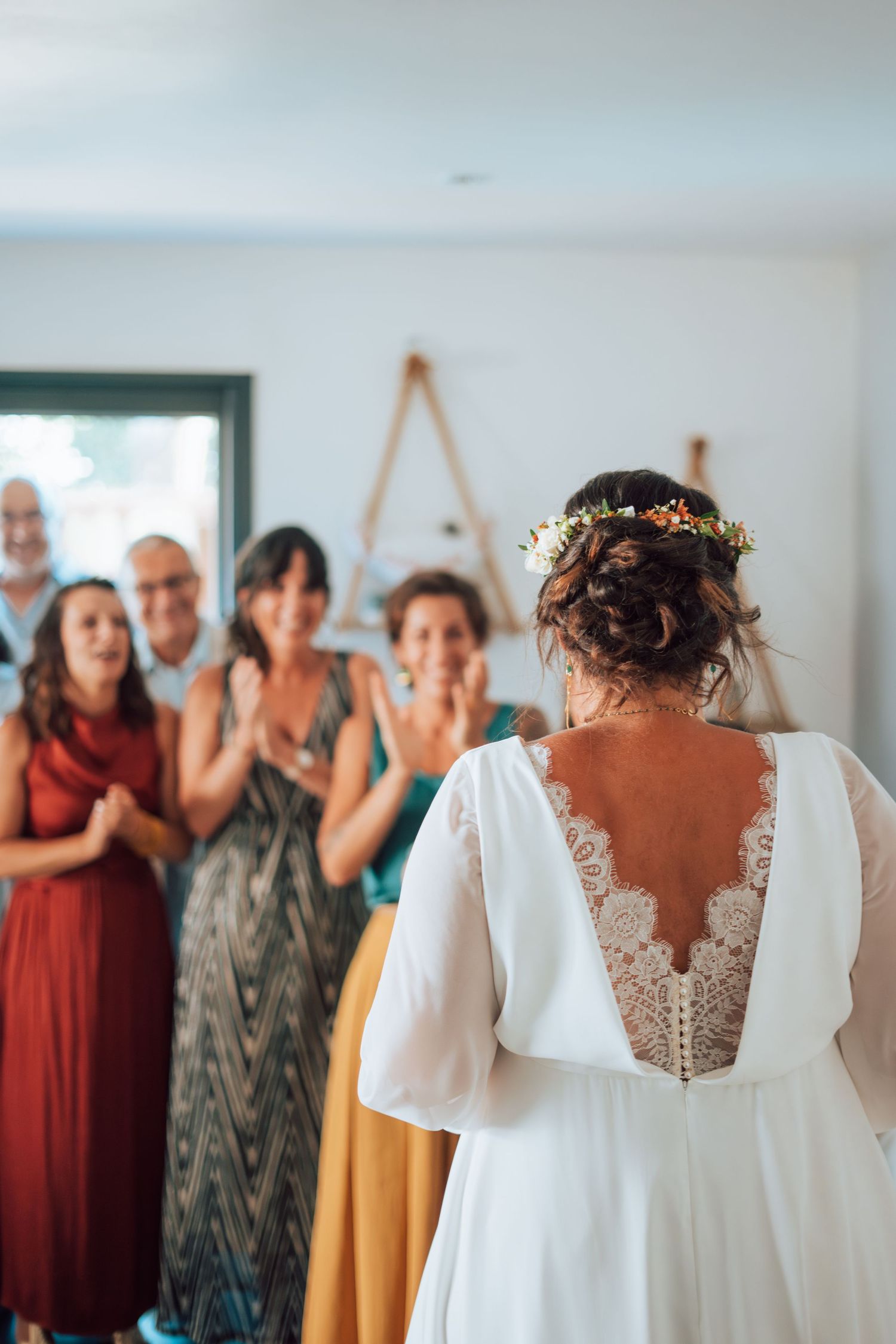 Bride in white lace-back gown with flower crown receives applause from wedding guests.