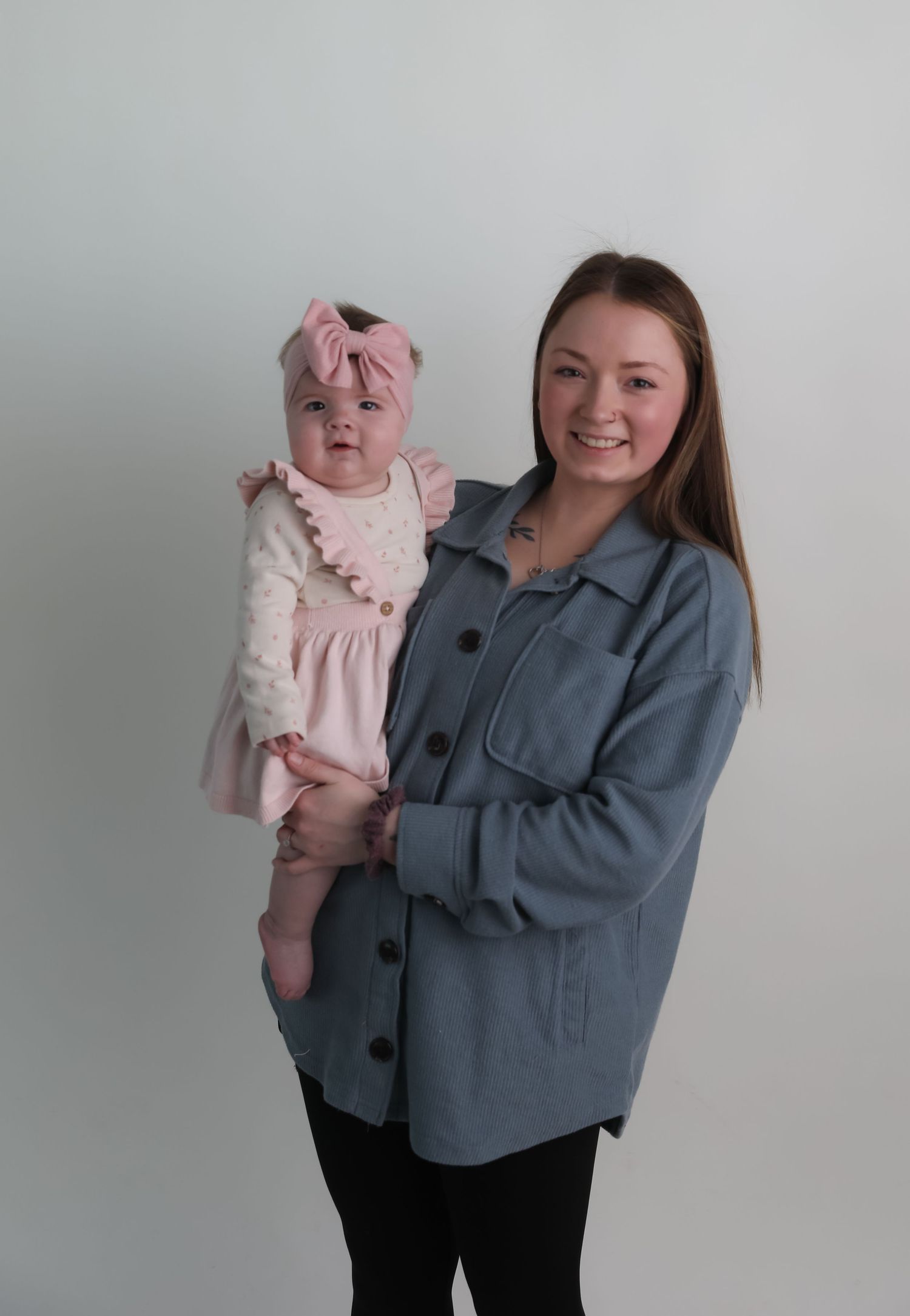 A smiling young mother holds her baby girl dressed in pink in a studio portrait.