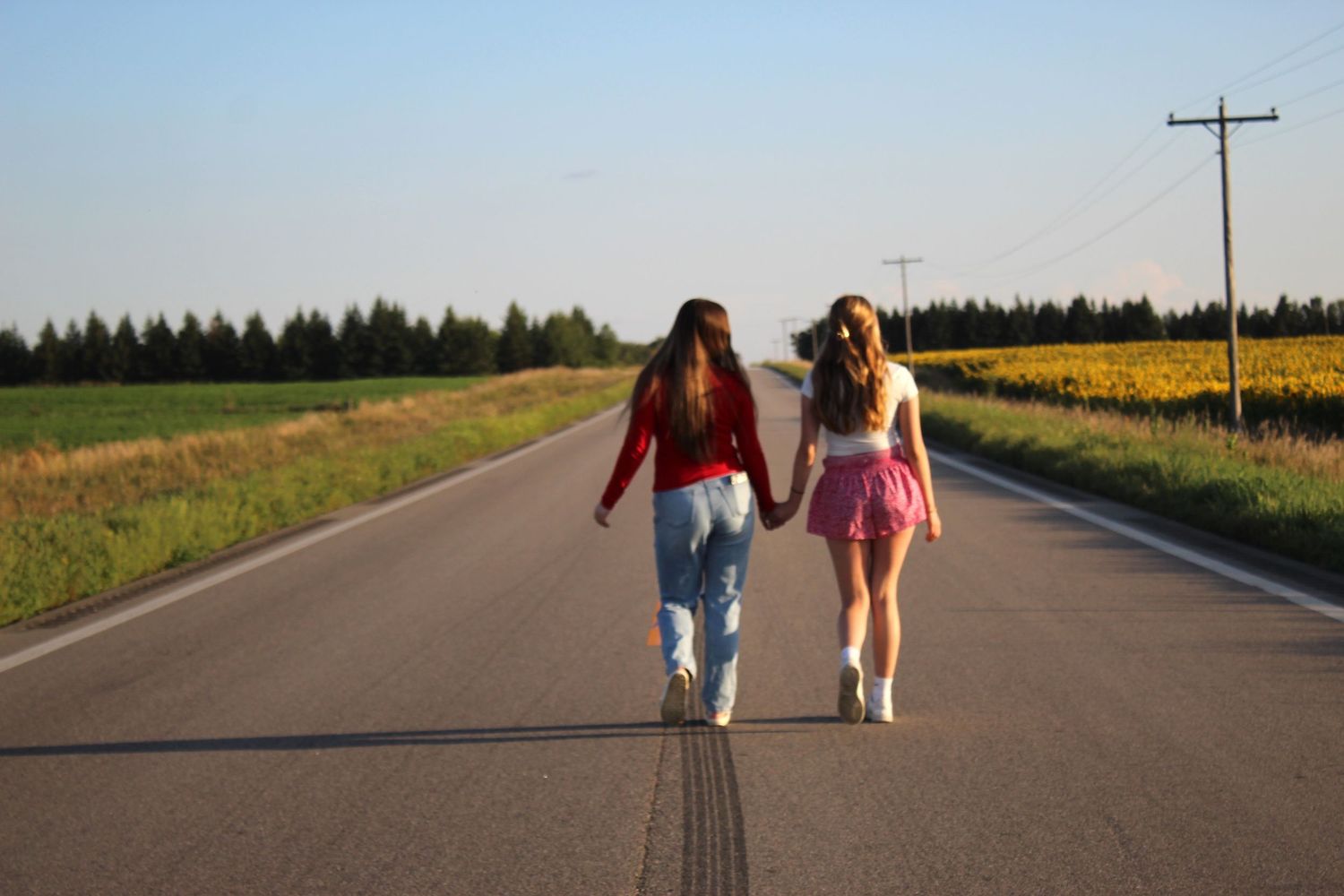 Two women in colorful outfits stroll down a rural road at sunset.