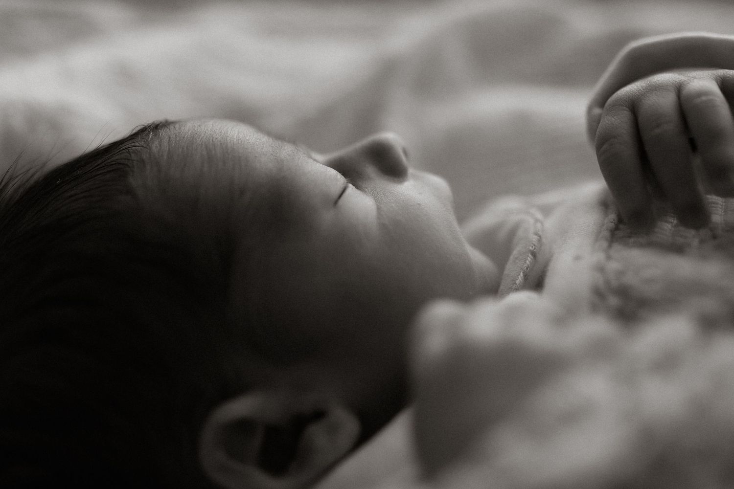 Black and white close-up of peaceful sleeping newborn baby lying on soft white blanket.