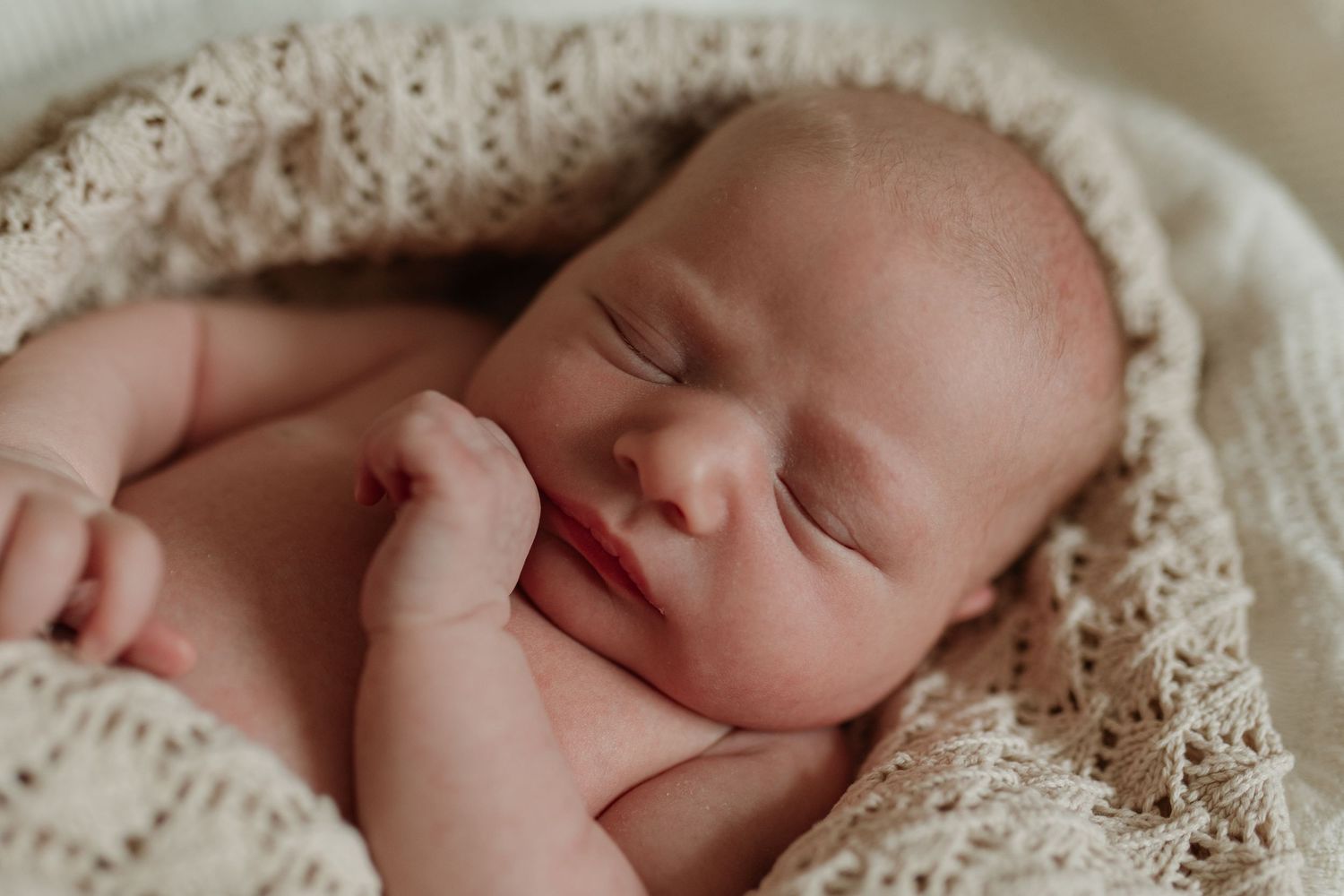 Peaceful sleeping newborn baby wrapped snugly in a soft cream knitted blanket.