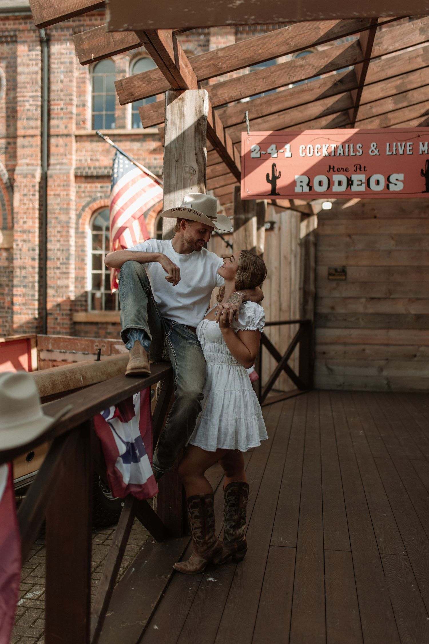 A couple shares a romantic kiss on a rustic Western saloon porch with American flag decor and cowboy boots.