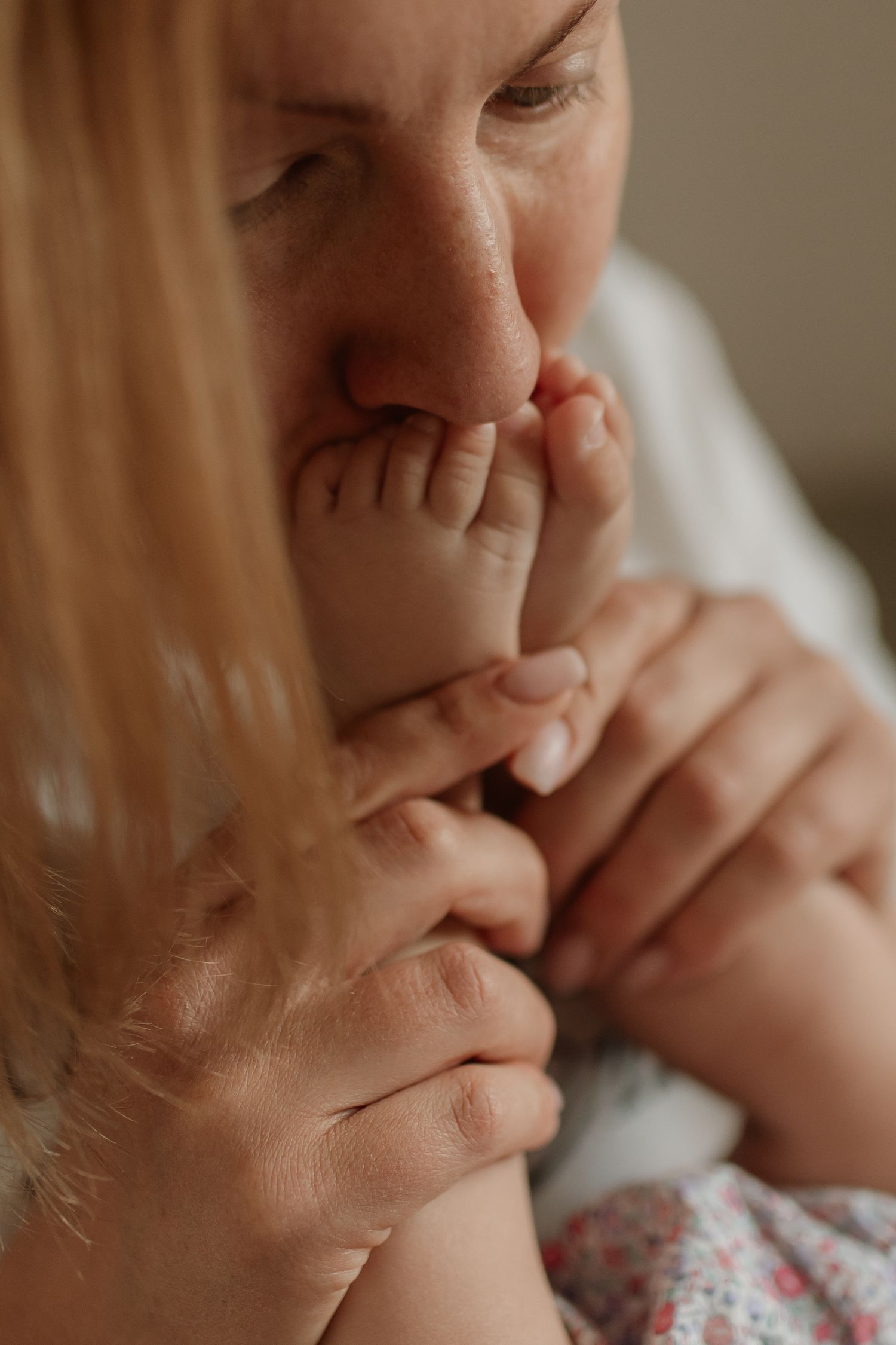 A mother gently kissing her newborns tiny feet in a tender close-up portrait.