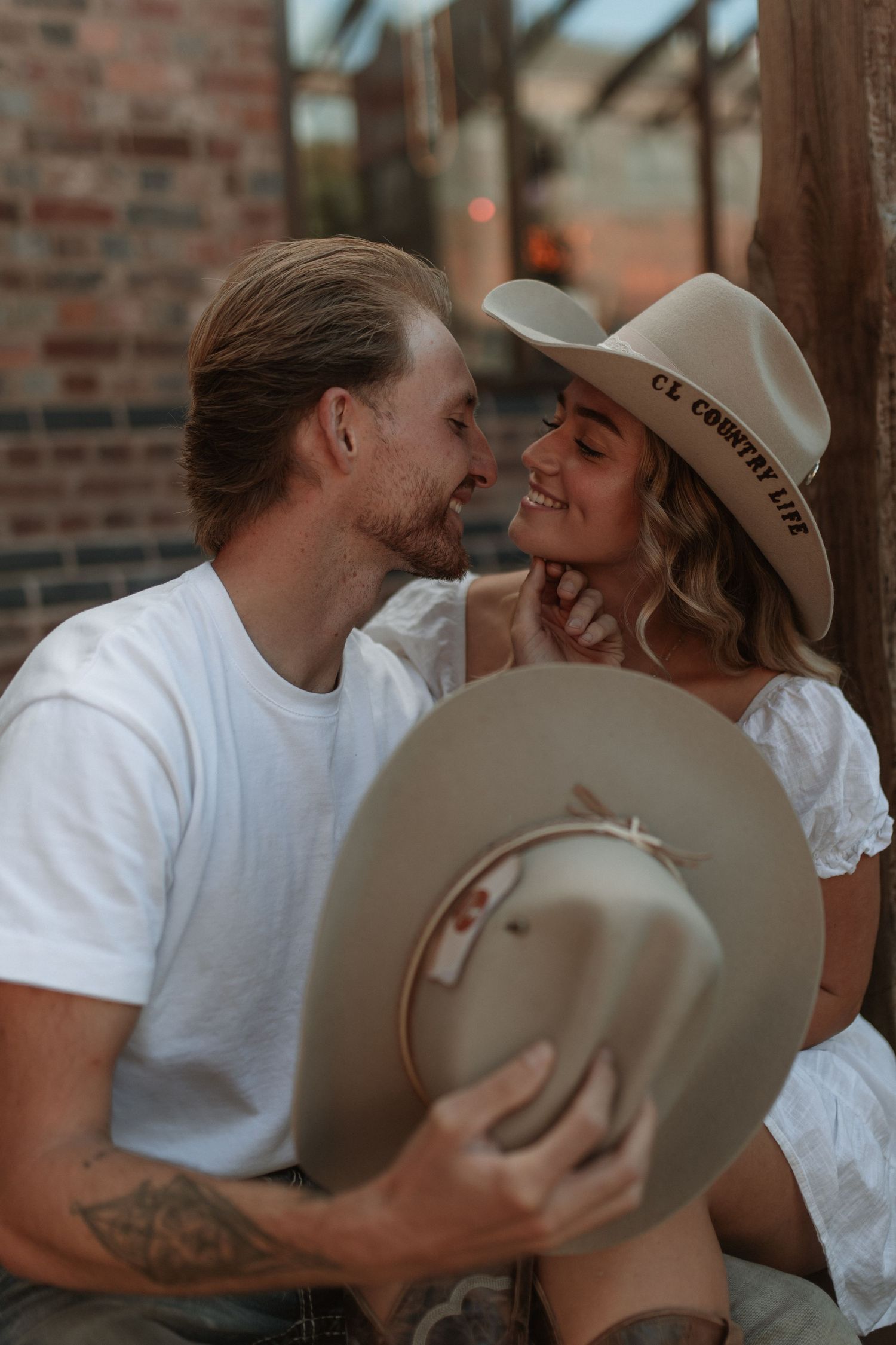 A couple sharing a romantic almost-kiss moment, the woman wearing a country life wide-brim hat outdoors.