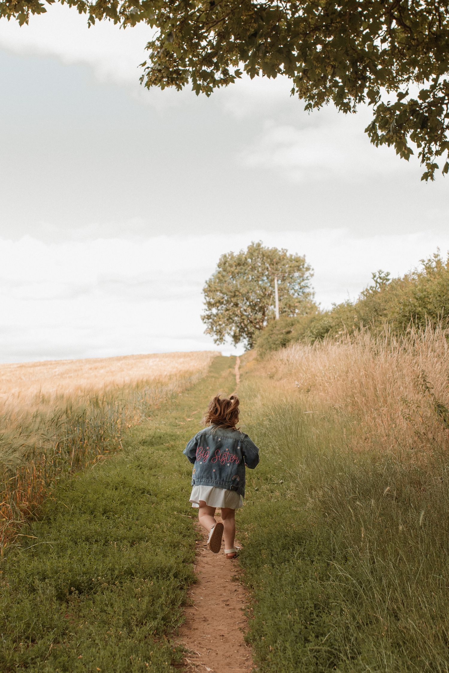 A young child in a floral jacket running along a countryside path toward a tree.