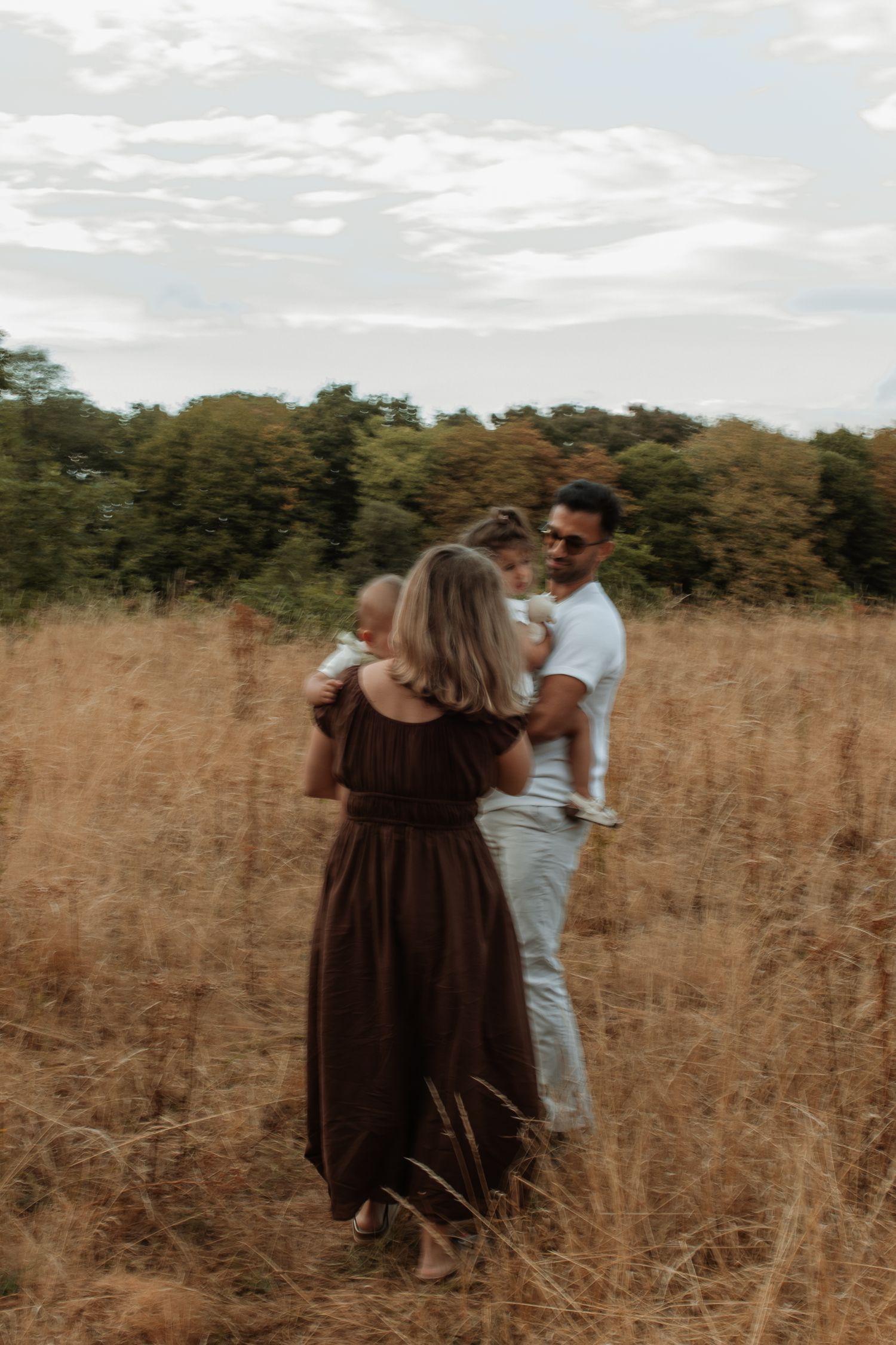 A couple stands in a golden field holding their two young children.