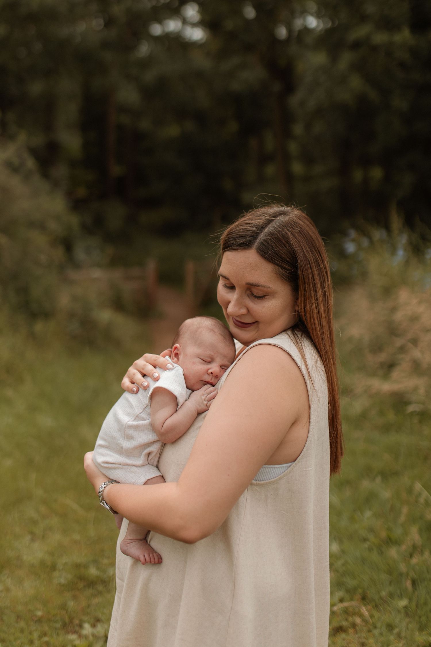 A mother tenderly holds her sleeping newborn baby outdoors in a green field.