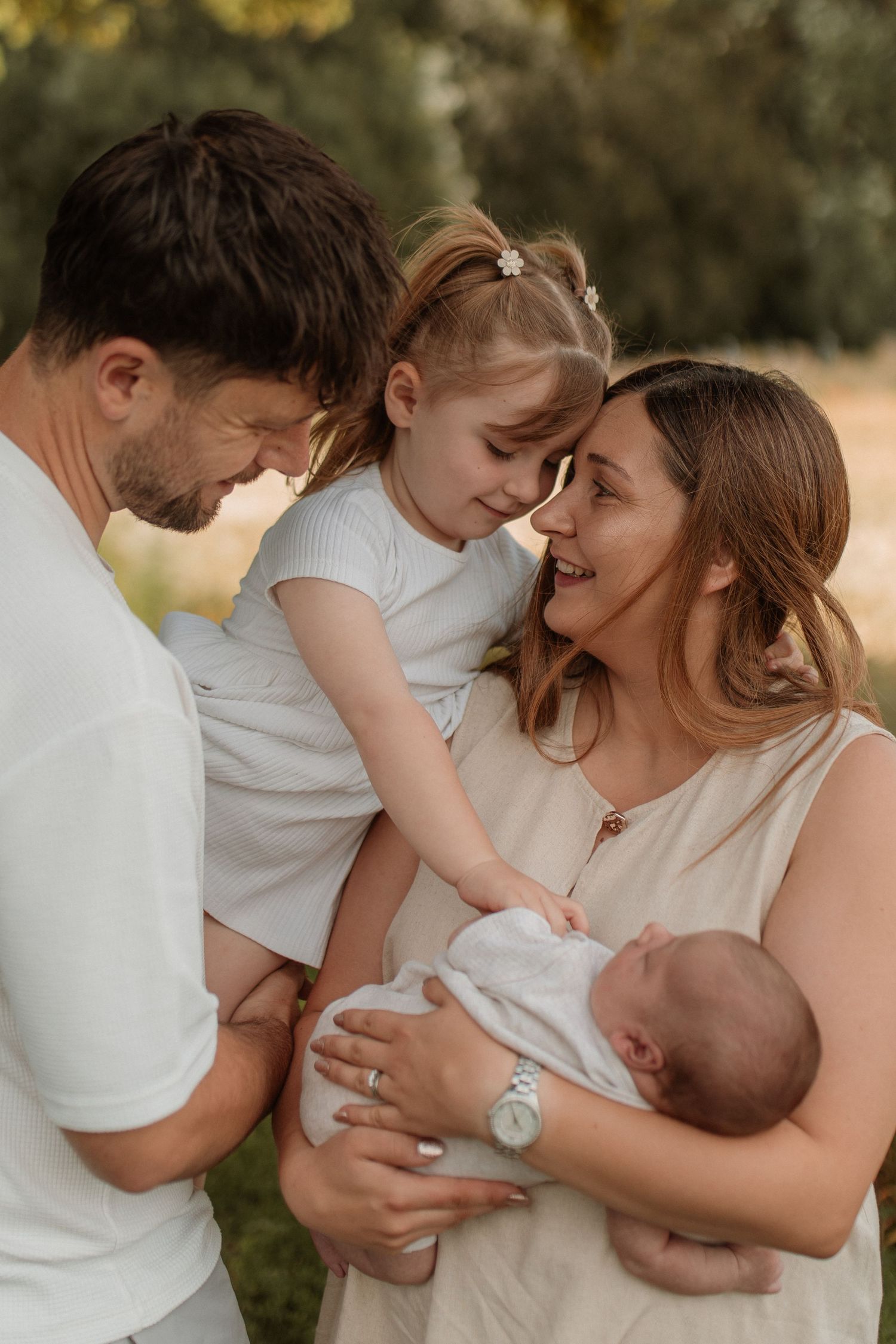 Happy family of four with toddler girl and newborn baby sharing joyful moment outdoors.