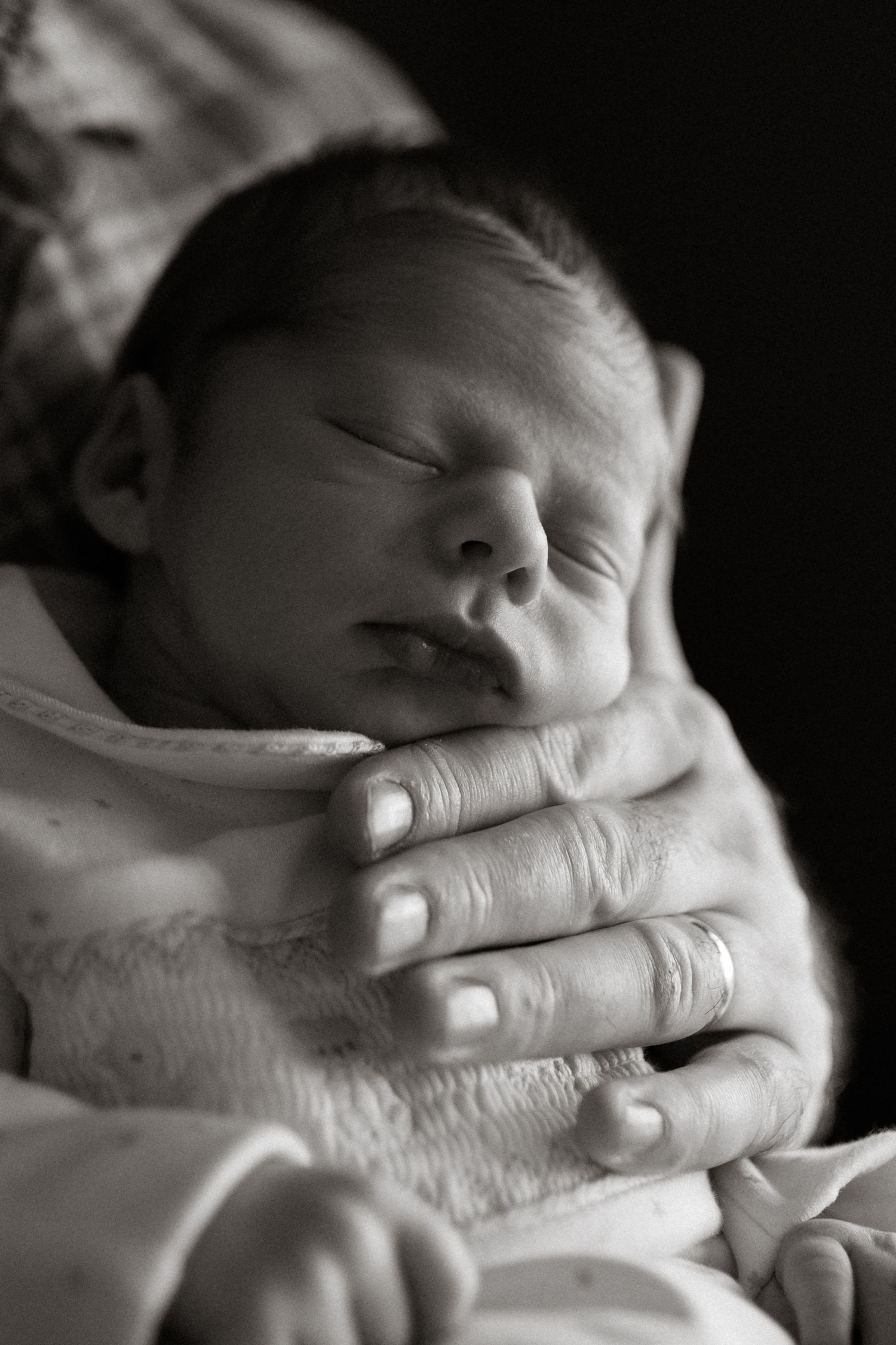 Black and white portrait of sleeping newborn baby cradled in fathers hands.