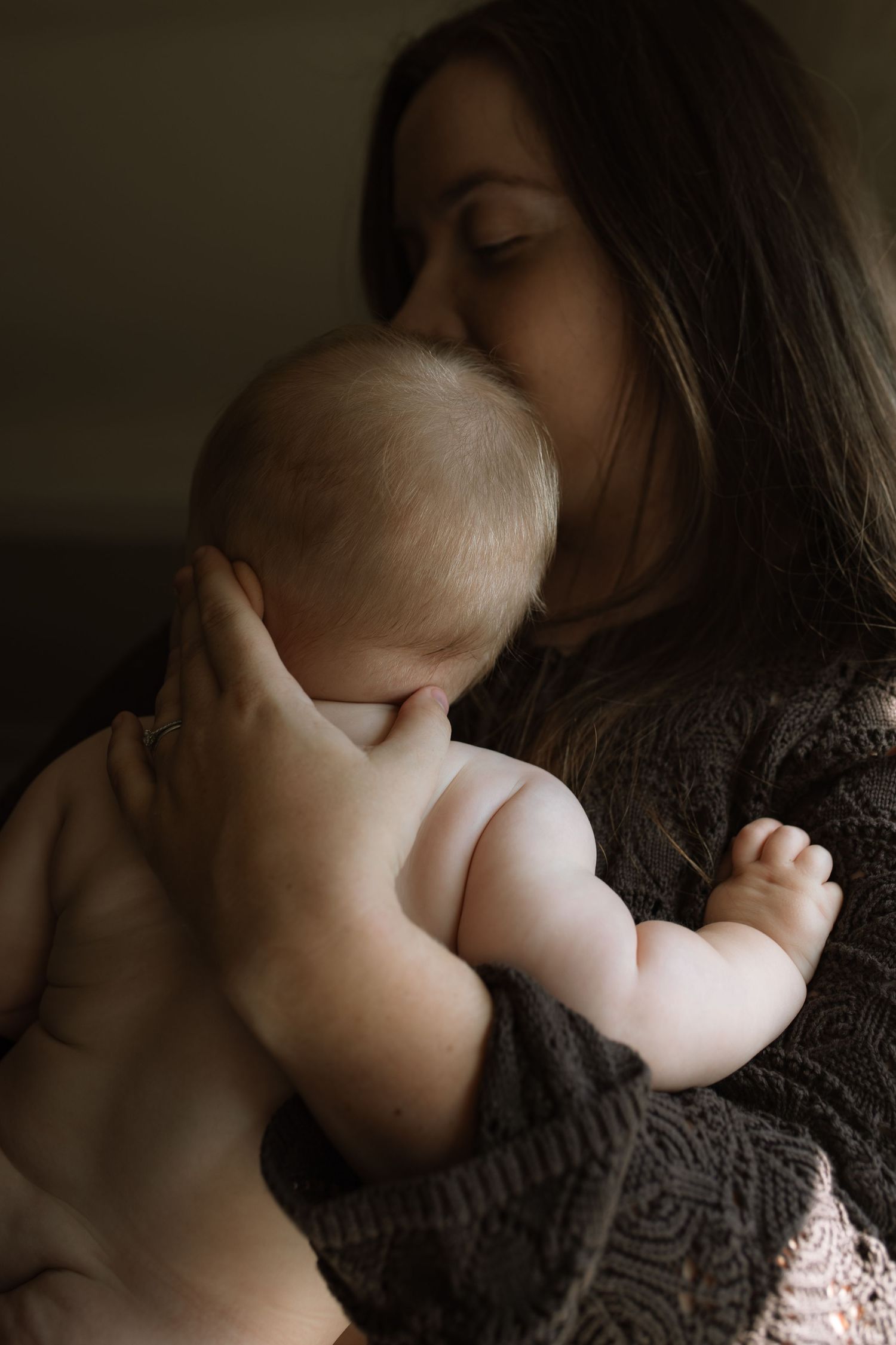 Mother tenderly kissing her newborn baby in a softly lit, intimate indoor setting.