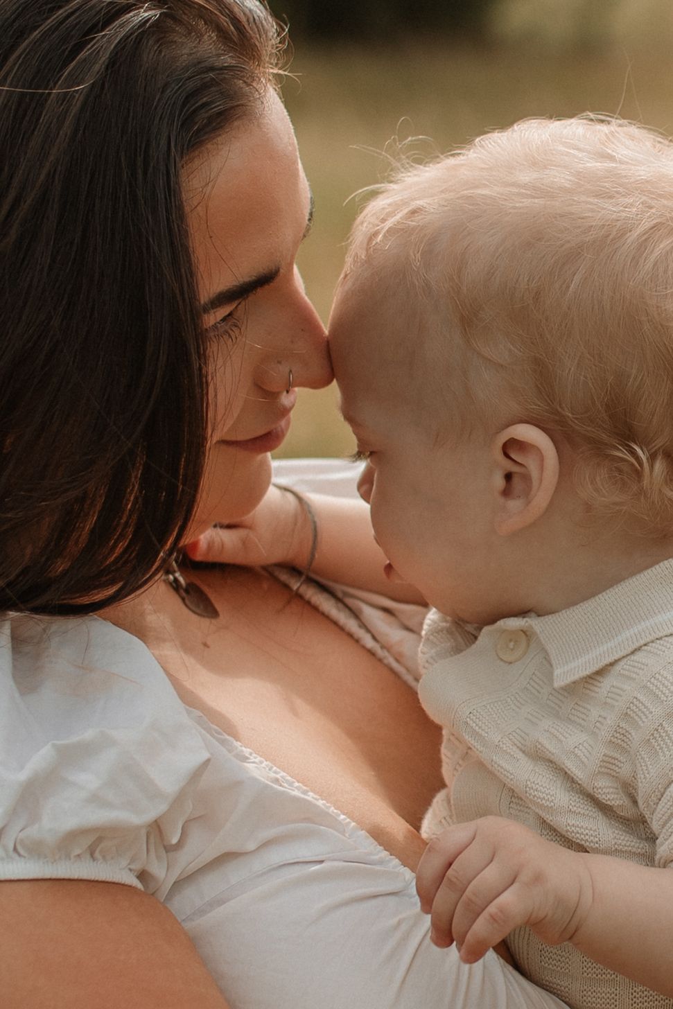 An intimate close-up of a mother and baby touching noses affectionately in warm golden light.