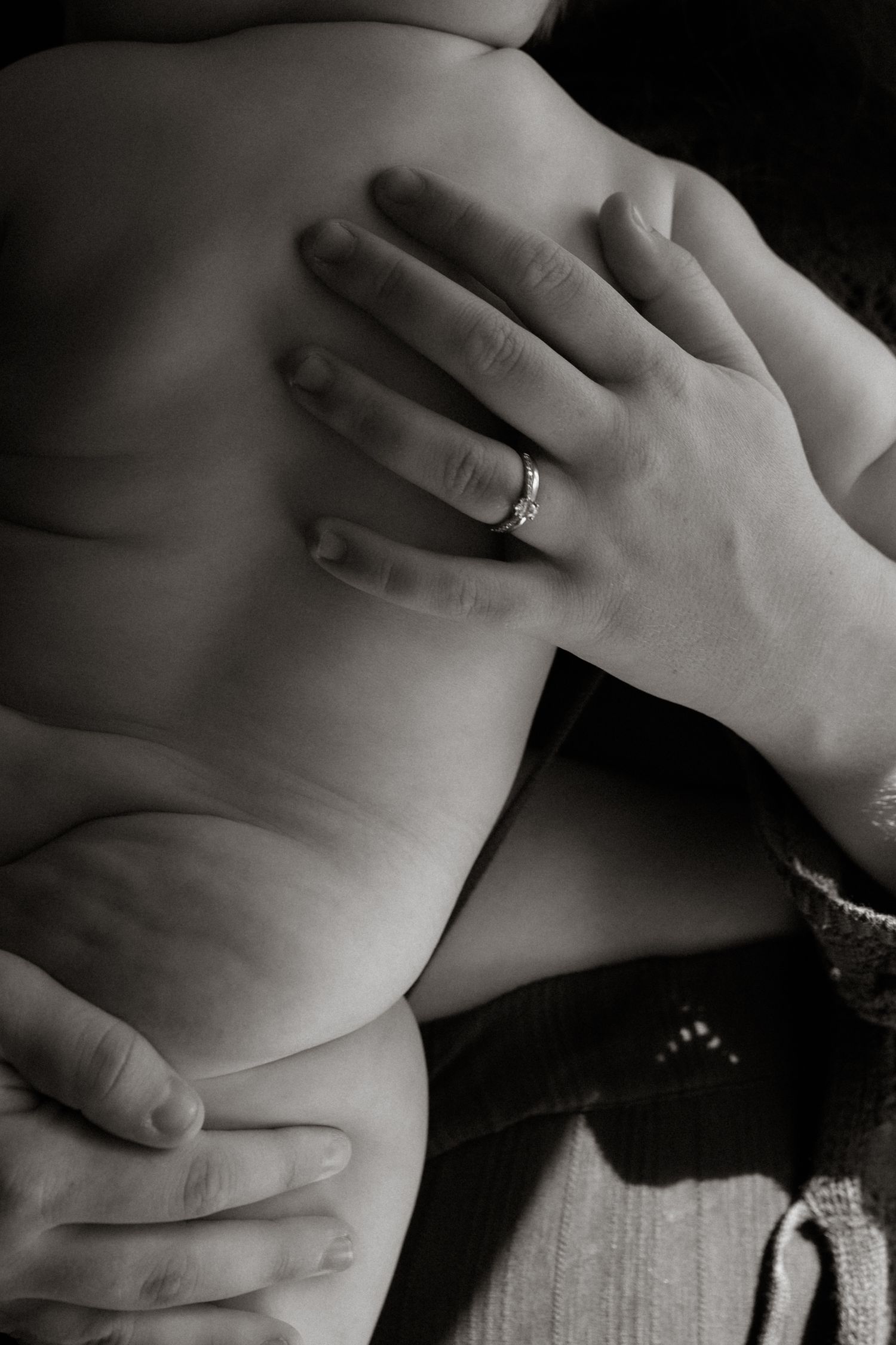 Black and white close-up of pregnant belly with hands gently cradling it, ring visible.