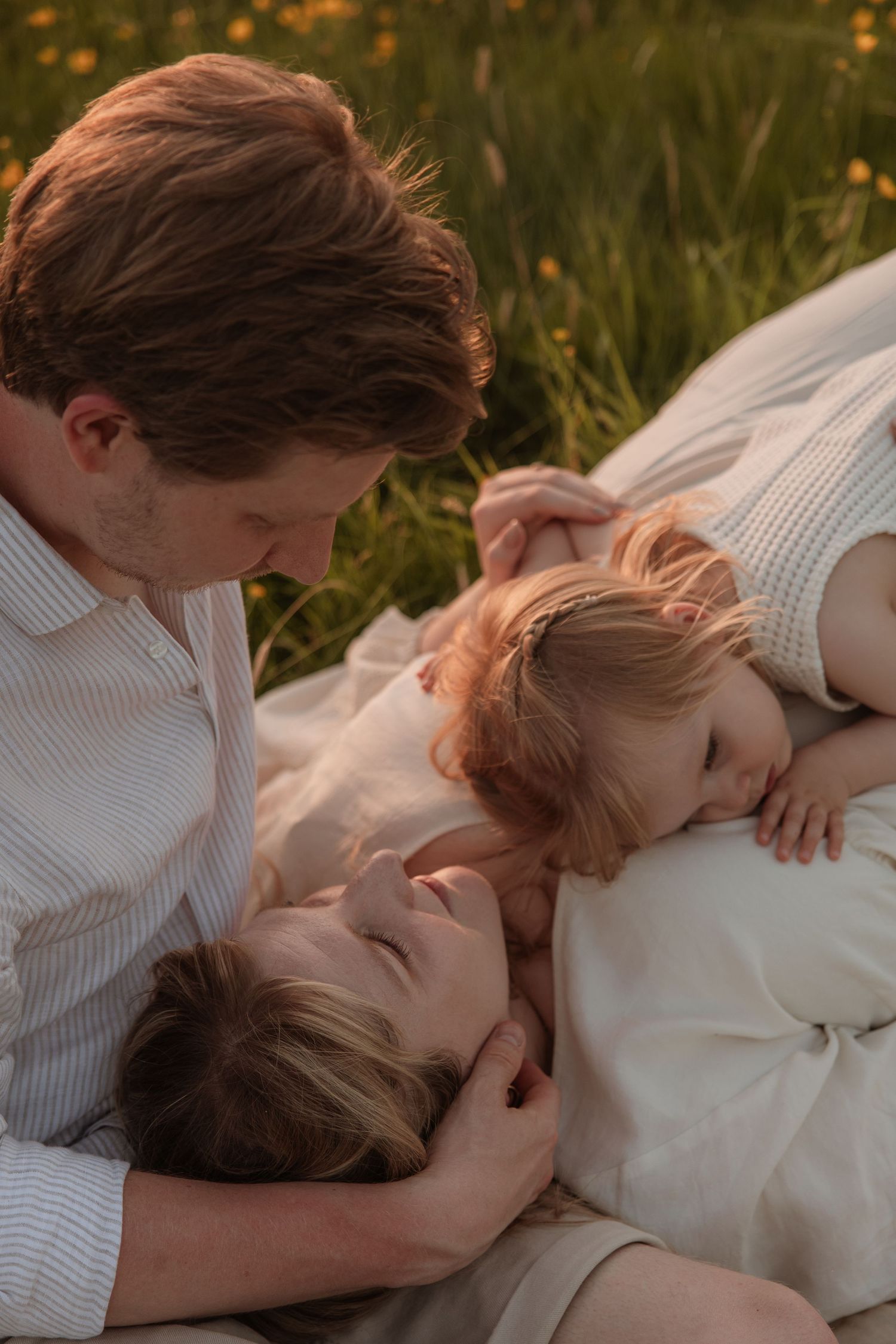 A father and mother lying in a meadow with their two young children at golden hour.