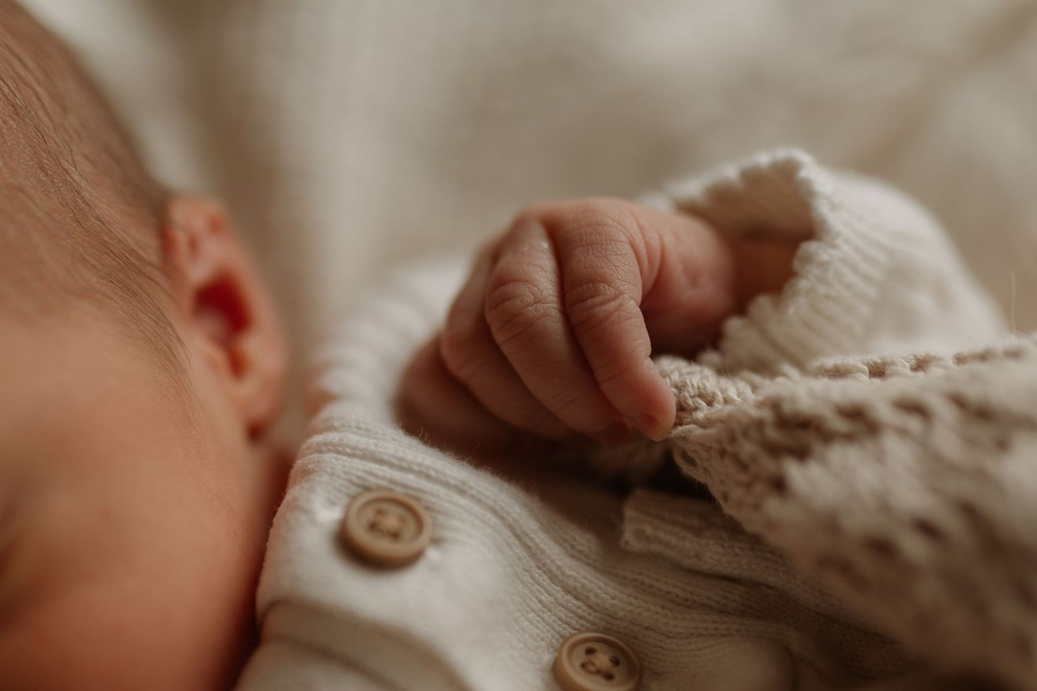 Close-up of a sleeping newborn baby's tiny hand clutching a soft knit blanket.