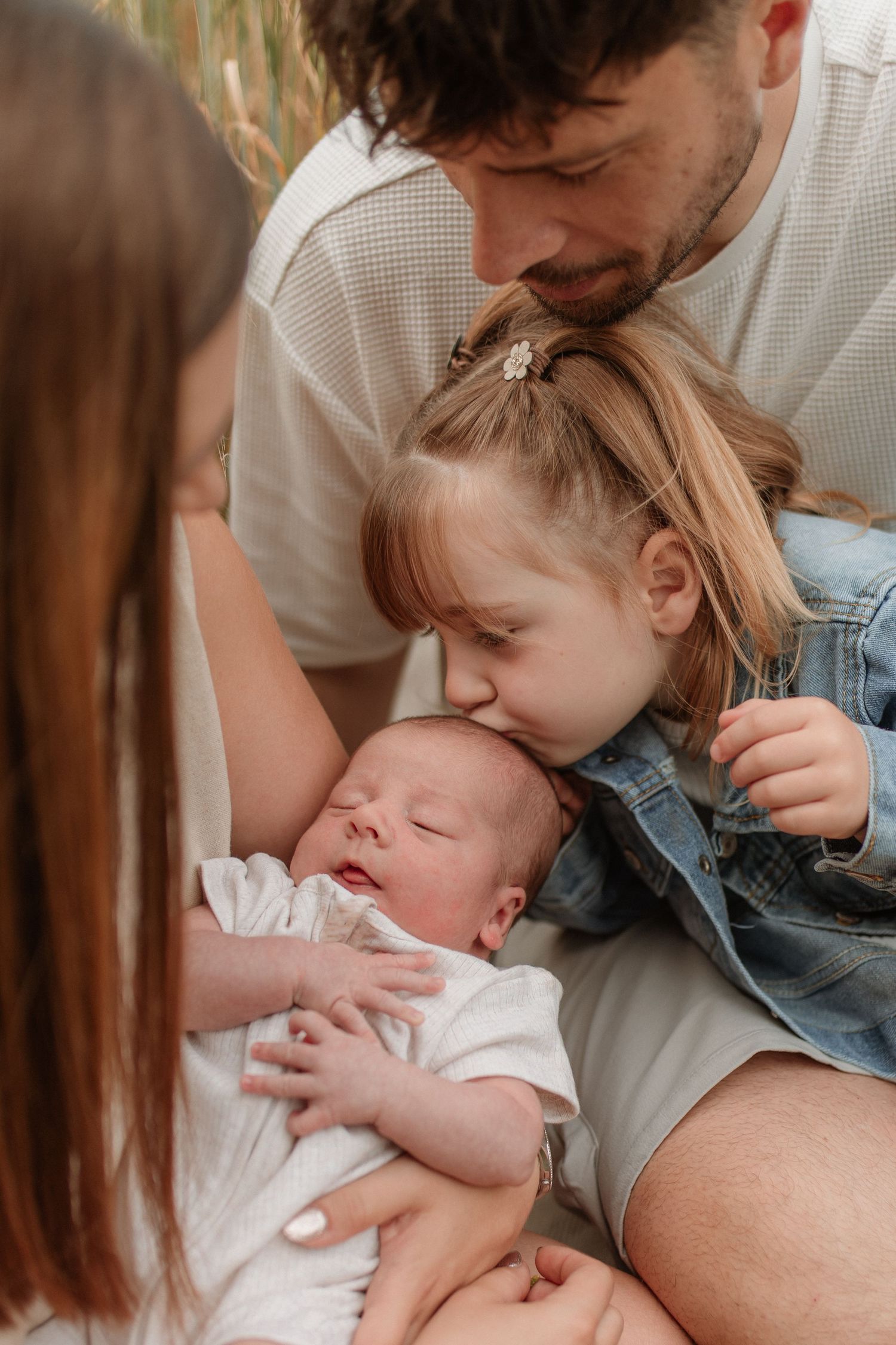 A loving family with father, young daughter, and mother admiring their newborn baby.