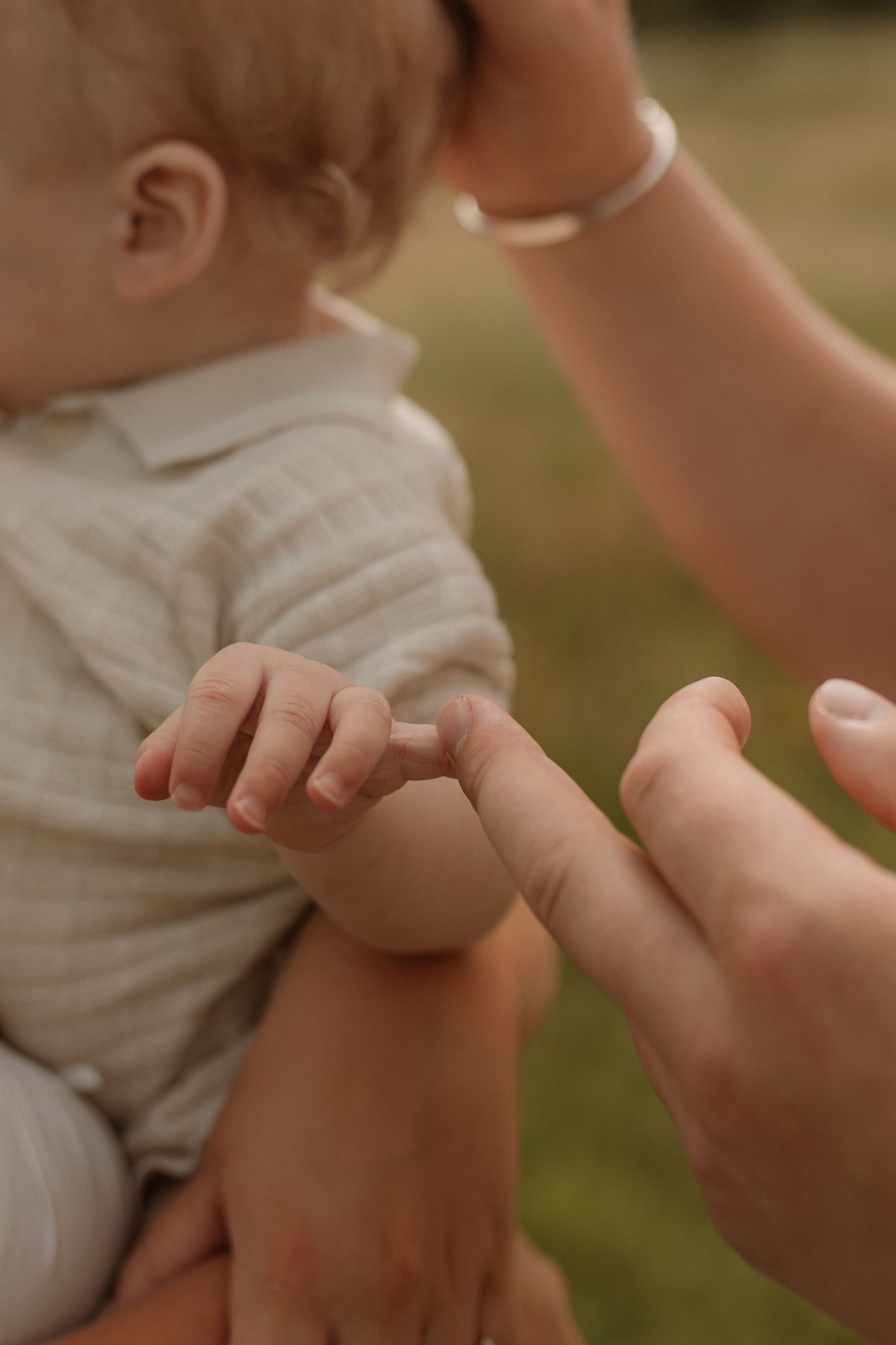 Close-up of a mother gently holding her baby's tiny hand outdoors in natural light.