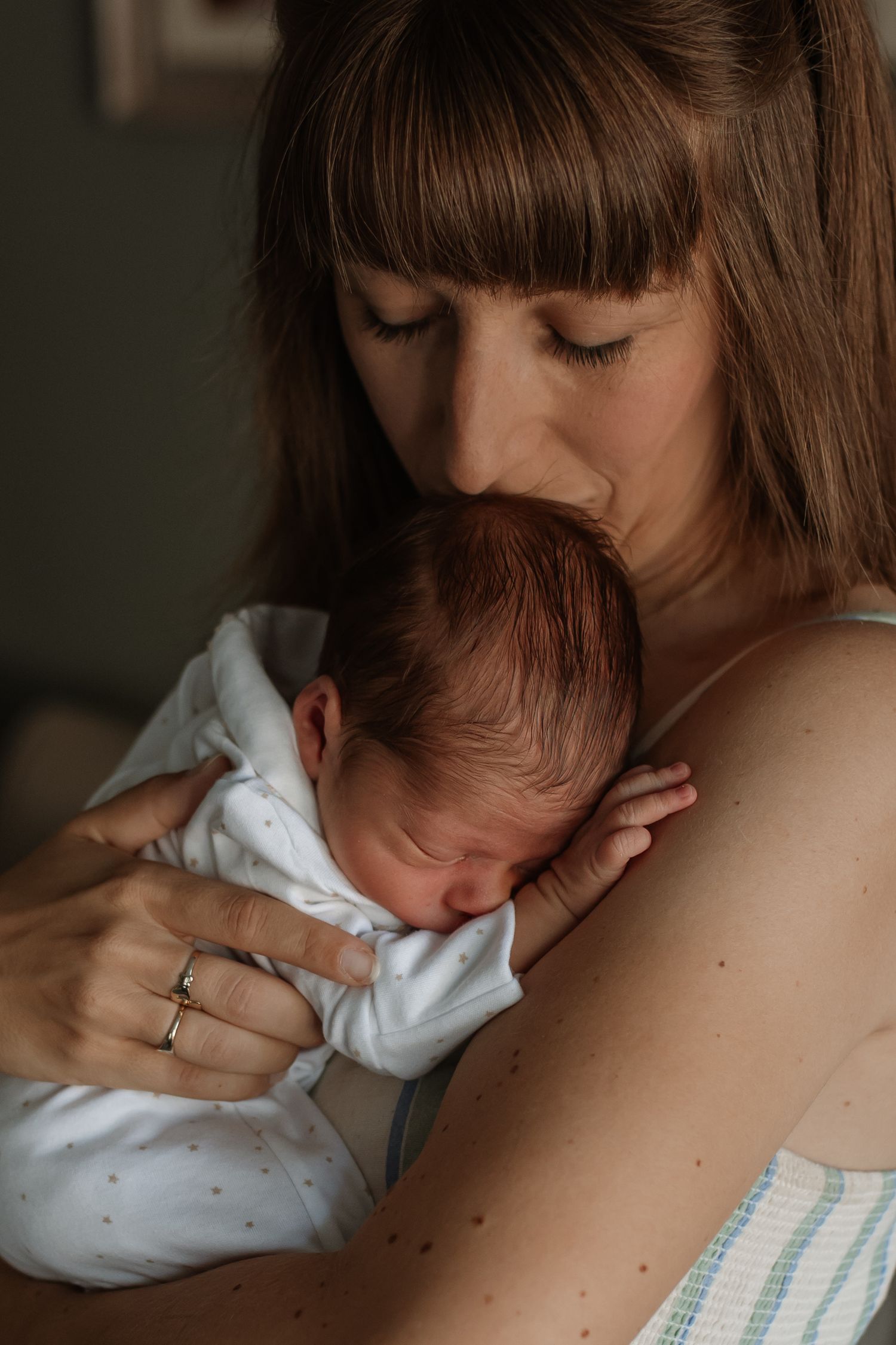Tender moment of mother kissing her newborn babys head while holding them close.
