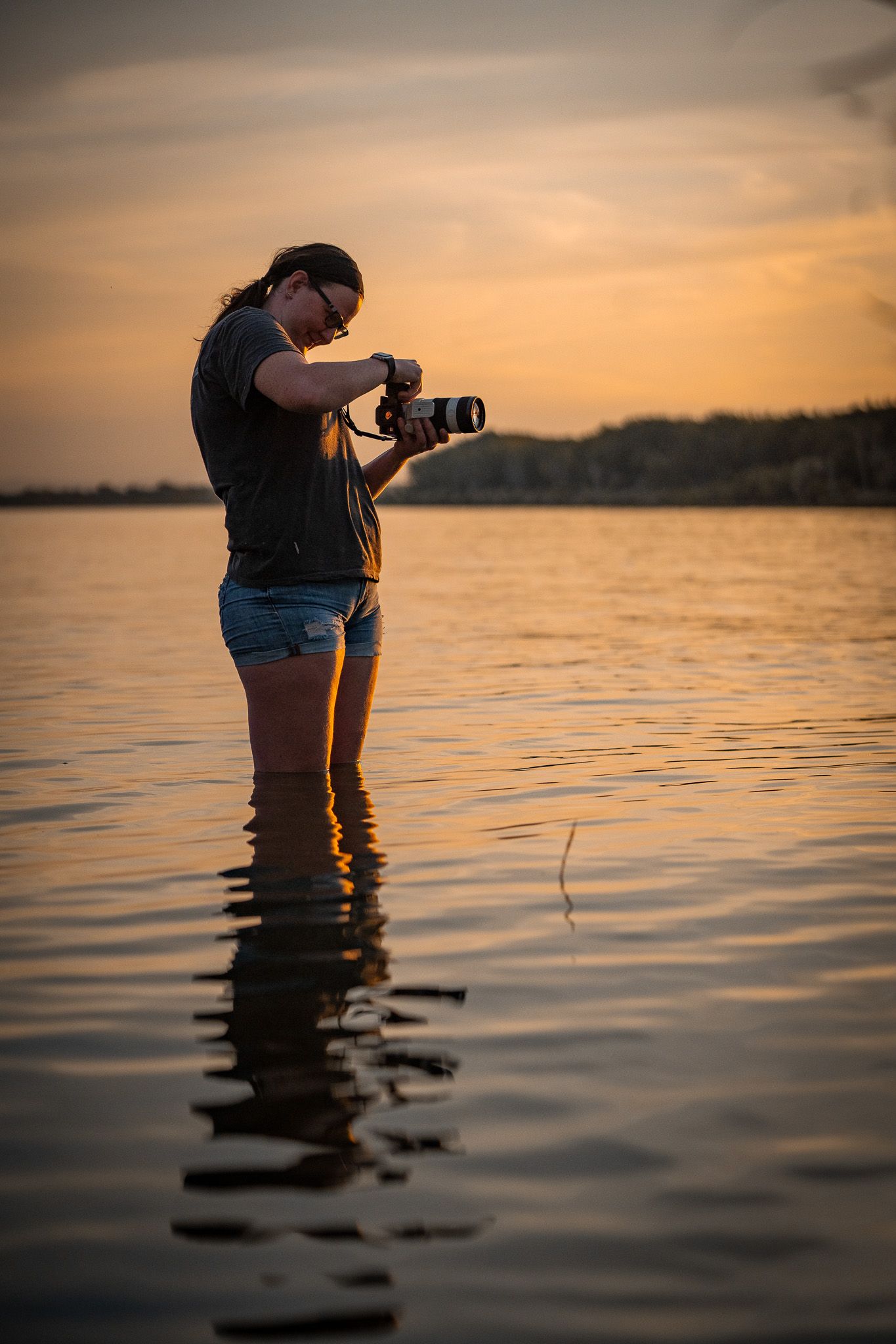 Carlleen of Double C Photography standing in an Idaho lake with her camera at sunset