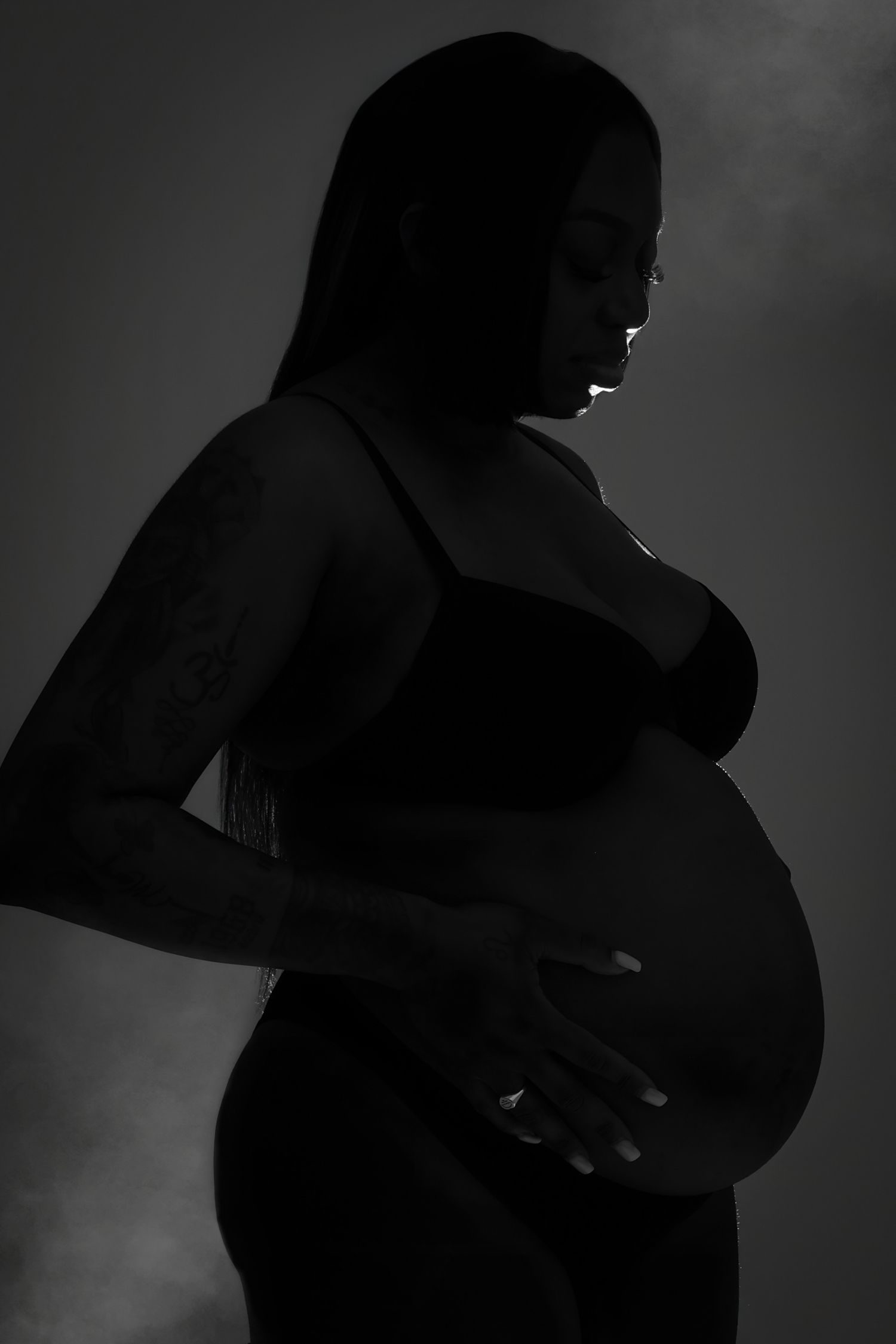 Black and white silhouette portrait of pregnant woman cradling baby bump in studio.