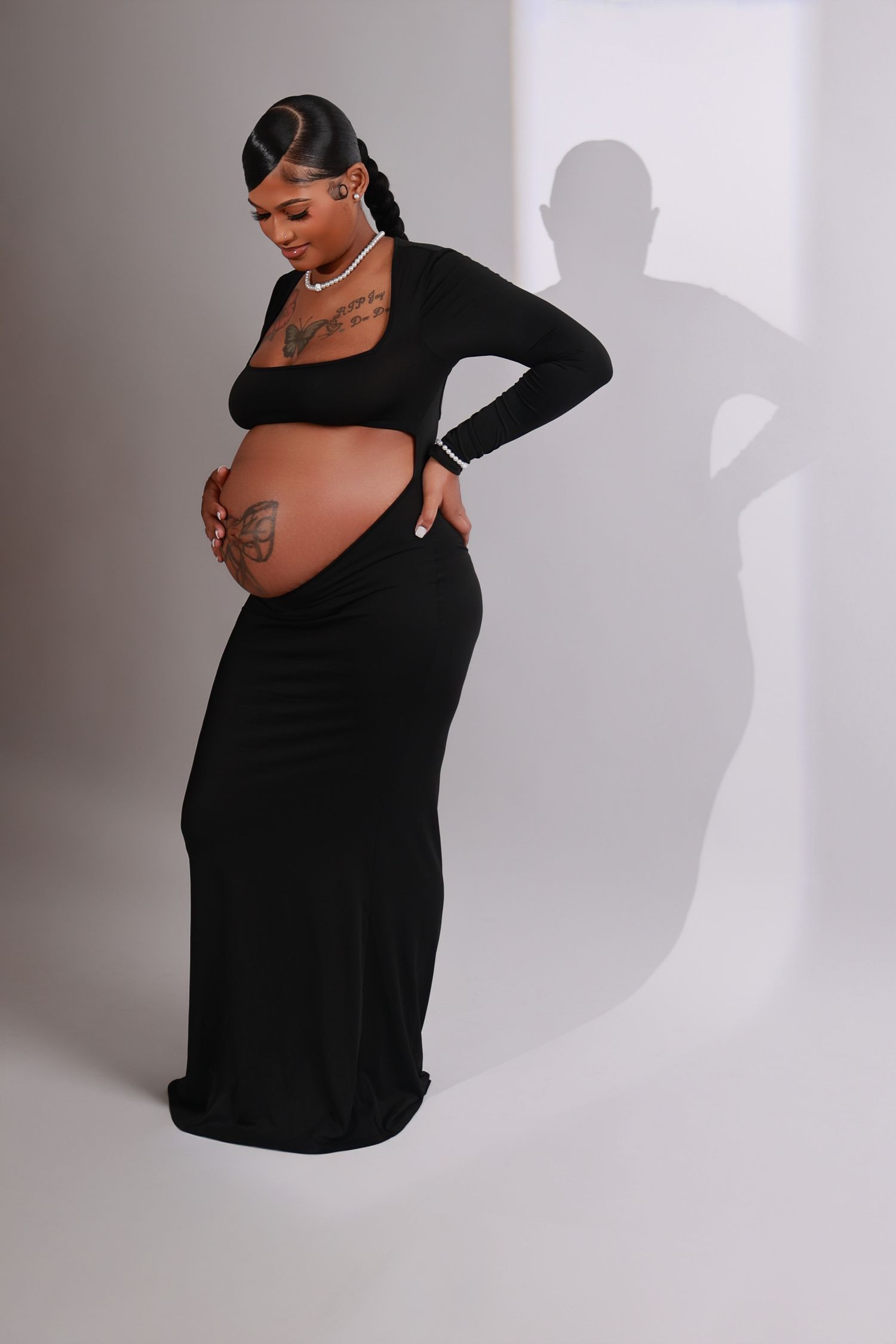Pregnant woman in black cutout maxi dress poses gracefully with her baby bump in studio.