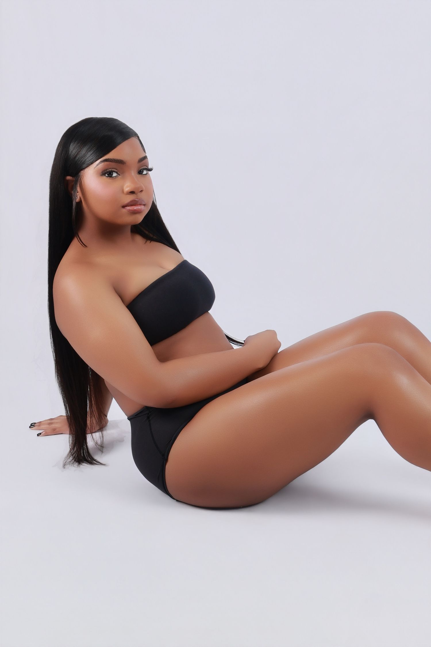 Young woman in black bandeau and bikini bottom poses on white studio floor.