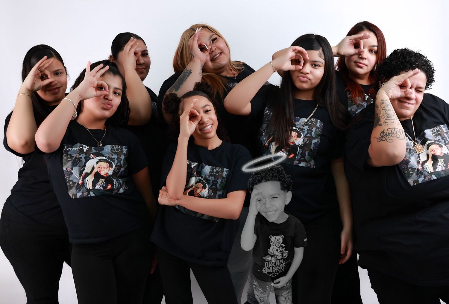 A group of women in matching black memorial shirts pose together making heart gestures with their hands.