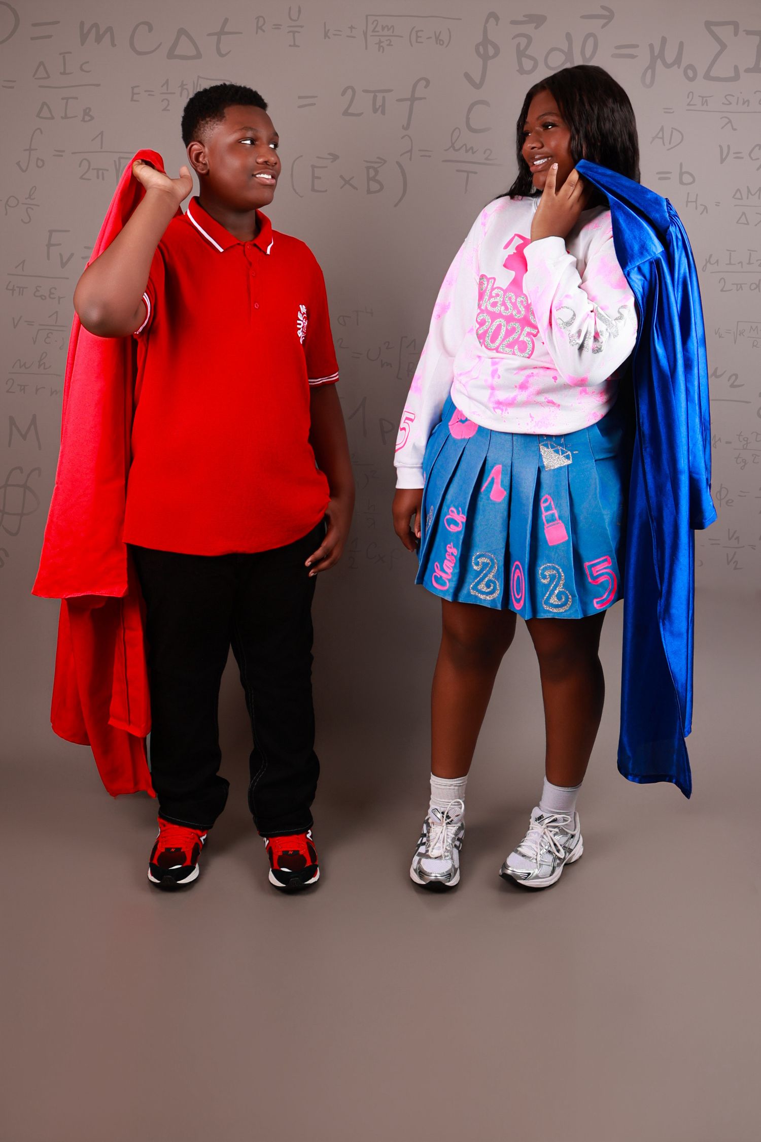 Two teens pose with graduation gowns in front of a chalkboard with math equations.