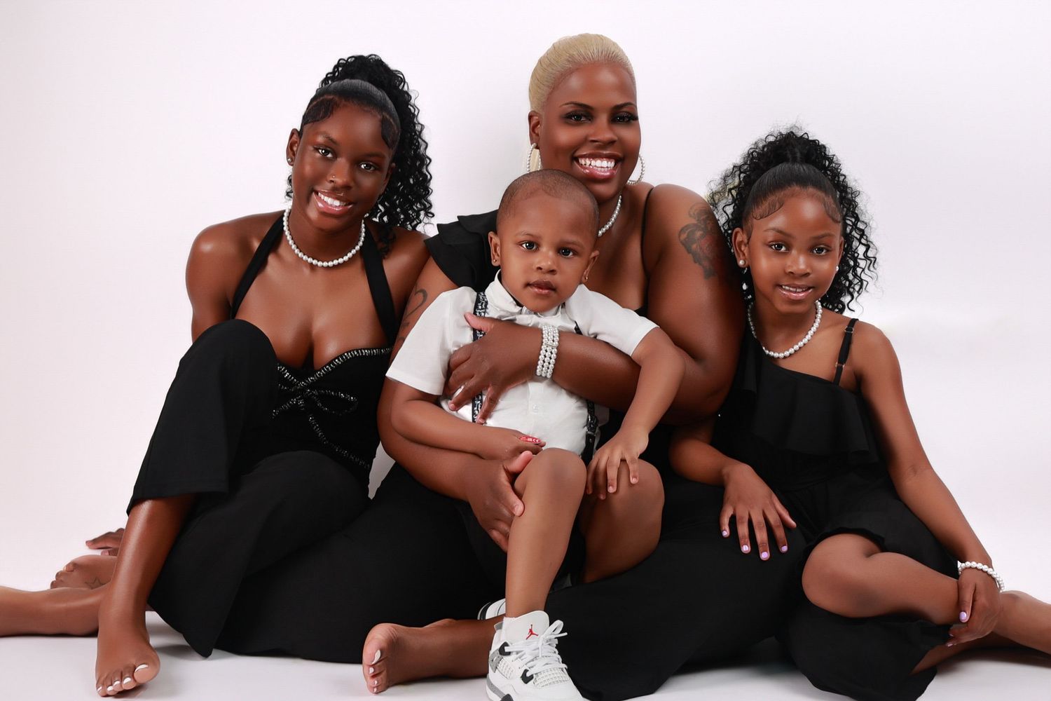 Mother in black dress poses with three children including baby boy in white studio.