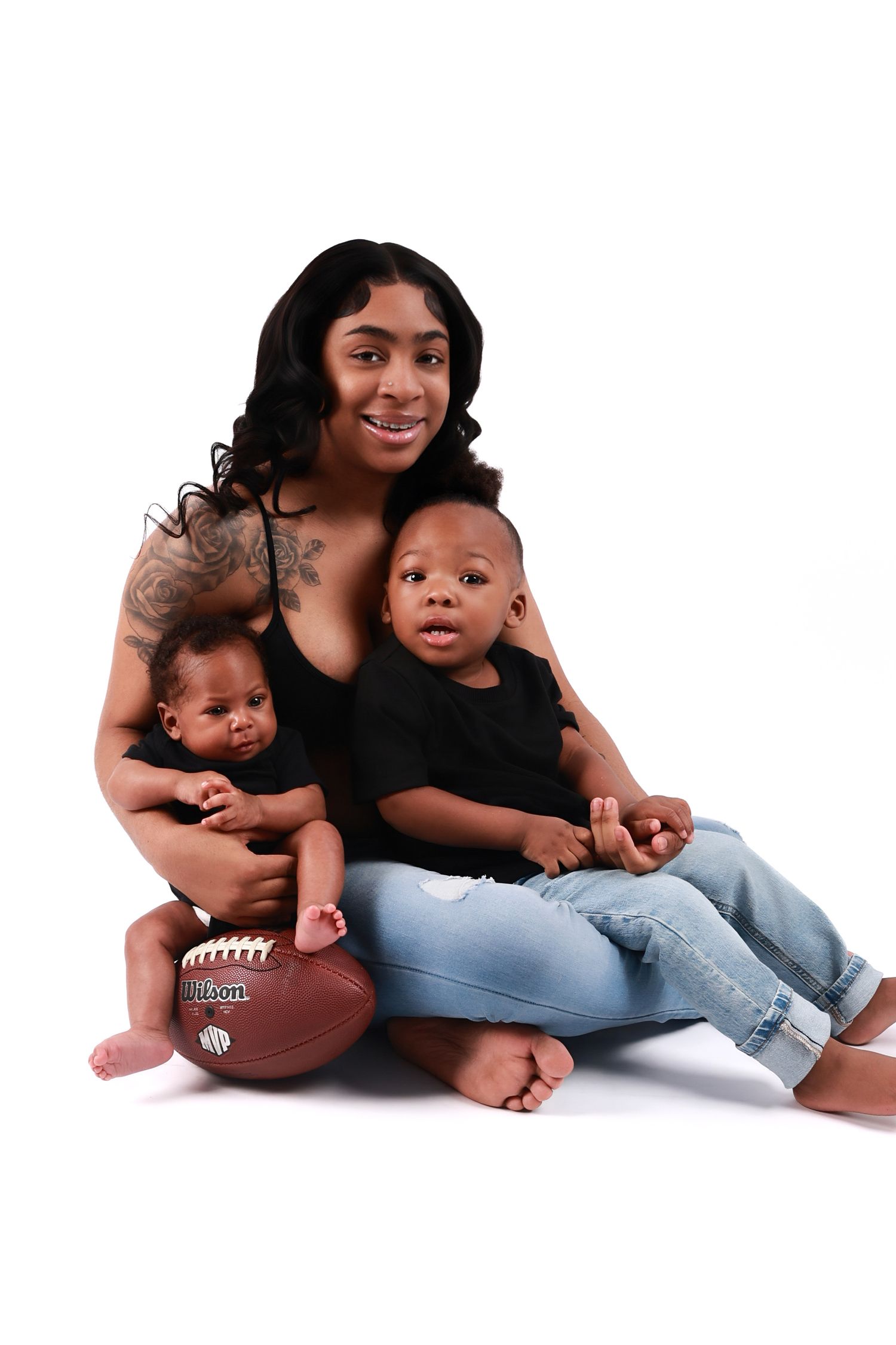 Smiling mother sitting with two young babies and a football on white background.
