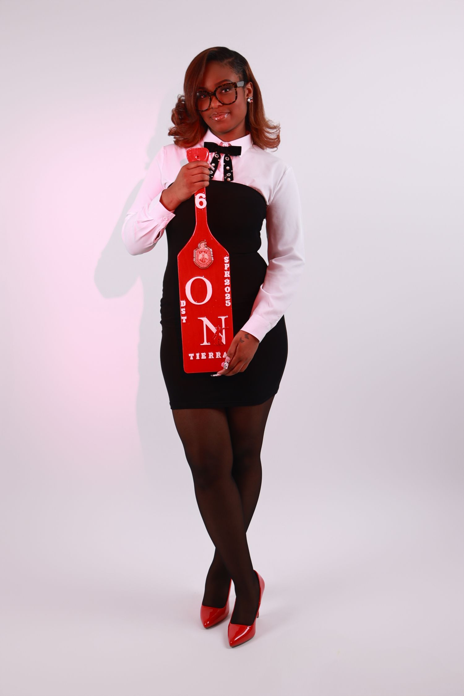 Woman in black dress holding red paddle with white shirt and red heels in studio photo.
