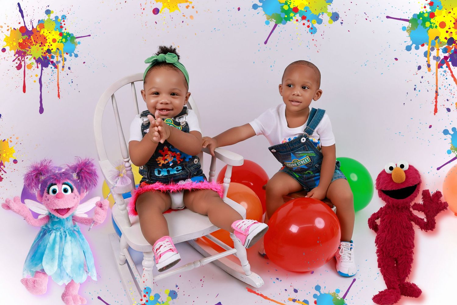 Two toddlers pose with Elmo and Abby Cadabby plush toys surrounded by colorful balloons in a festive Sesame Street birthday photo.