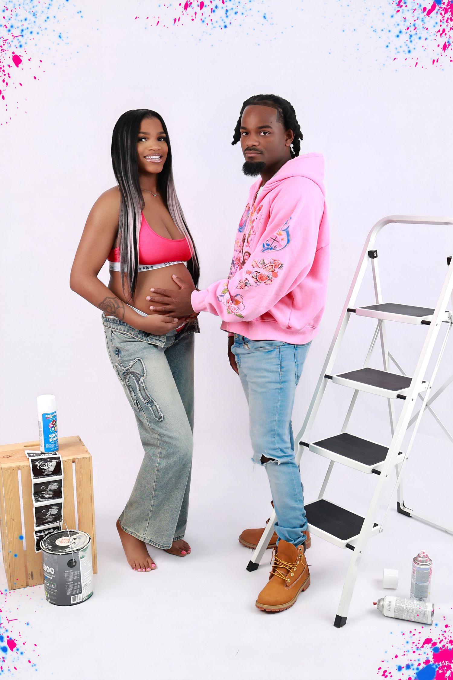Expecting couple poses with paint supplies and ladder for a gender reveal maternity photo shoot.