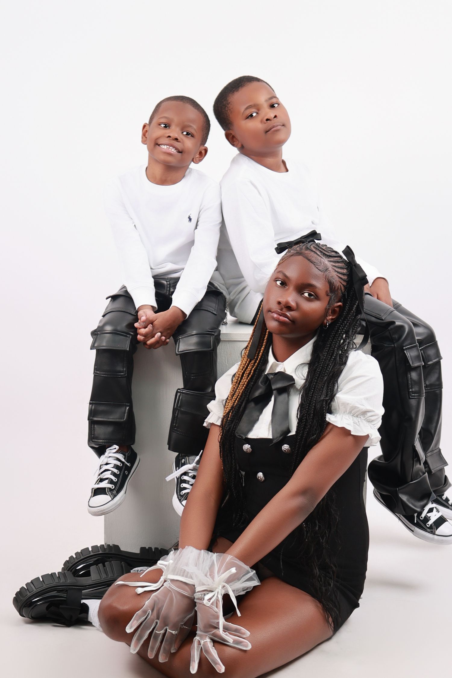 A girl sits on the floor while two boys perch behind her in a stylish black and white studio shoot.