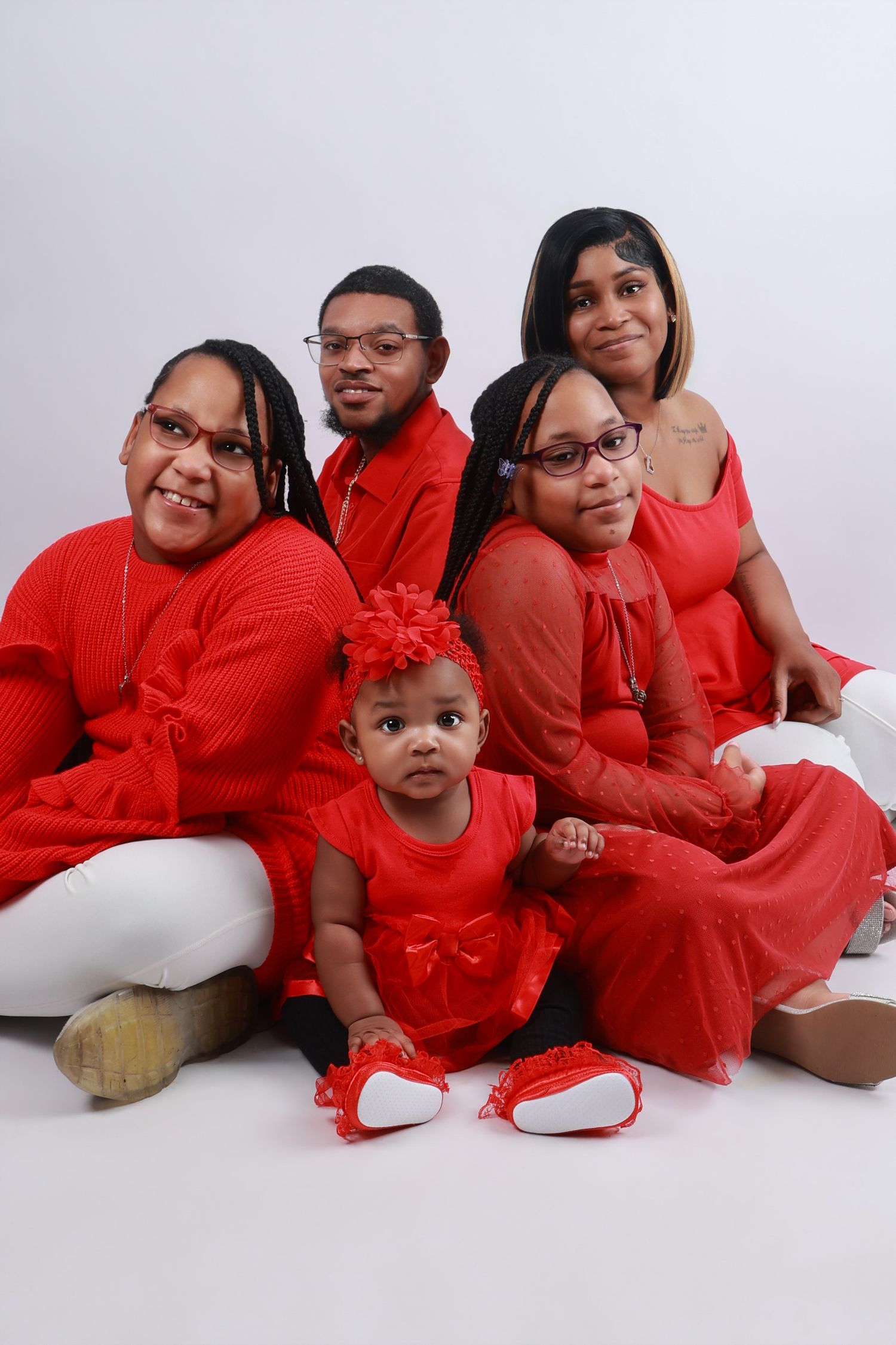 Family of five in matching red outfits poses together with a baby girl in a studio.