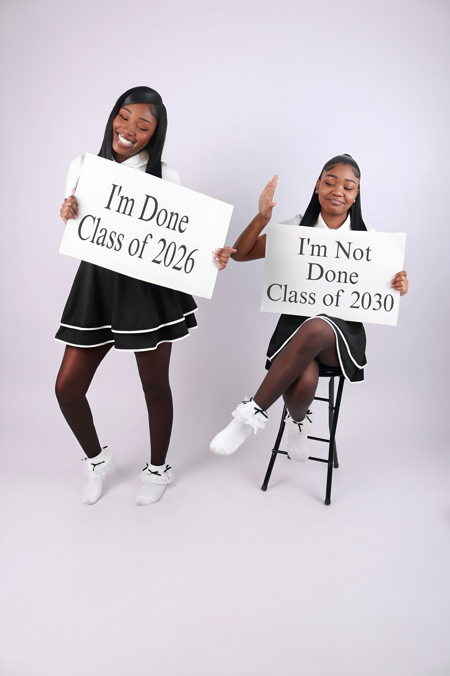 Two young women in matching black outfits hold signs reading Class of 2026 and Class of 2030.