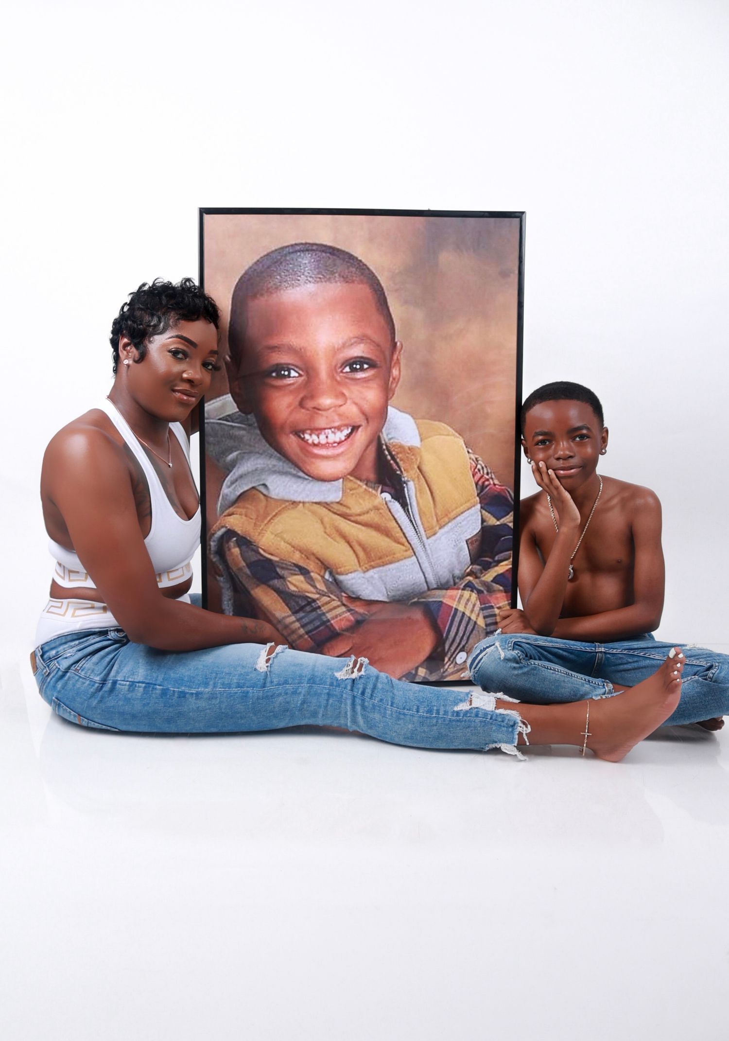 A mother and her son sit beside a large framed portrait of her first born son R.I.P Mari  young boy on white backdrop.