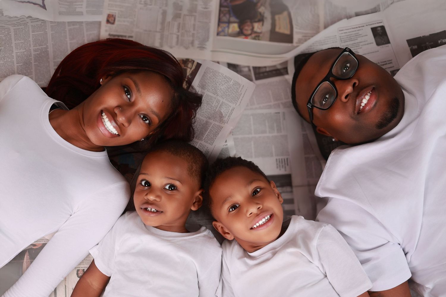 Family of four in white outfits smiling while lying on newspaper.
