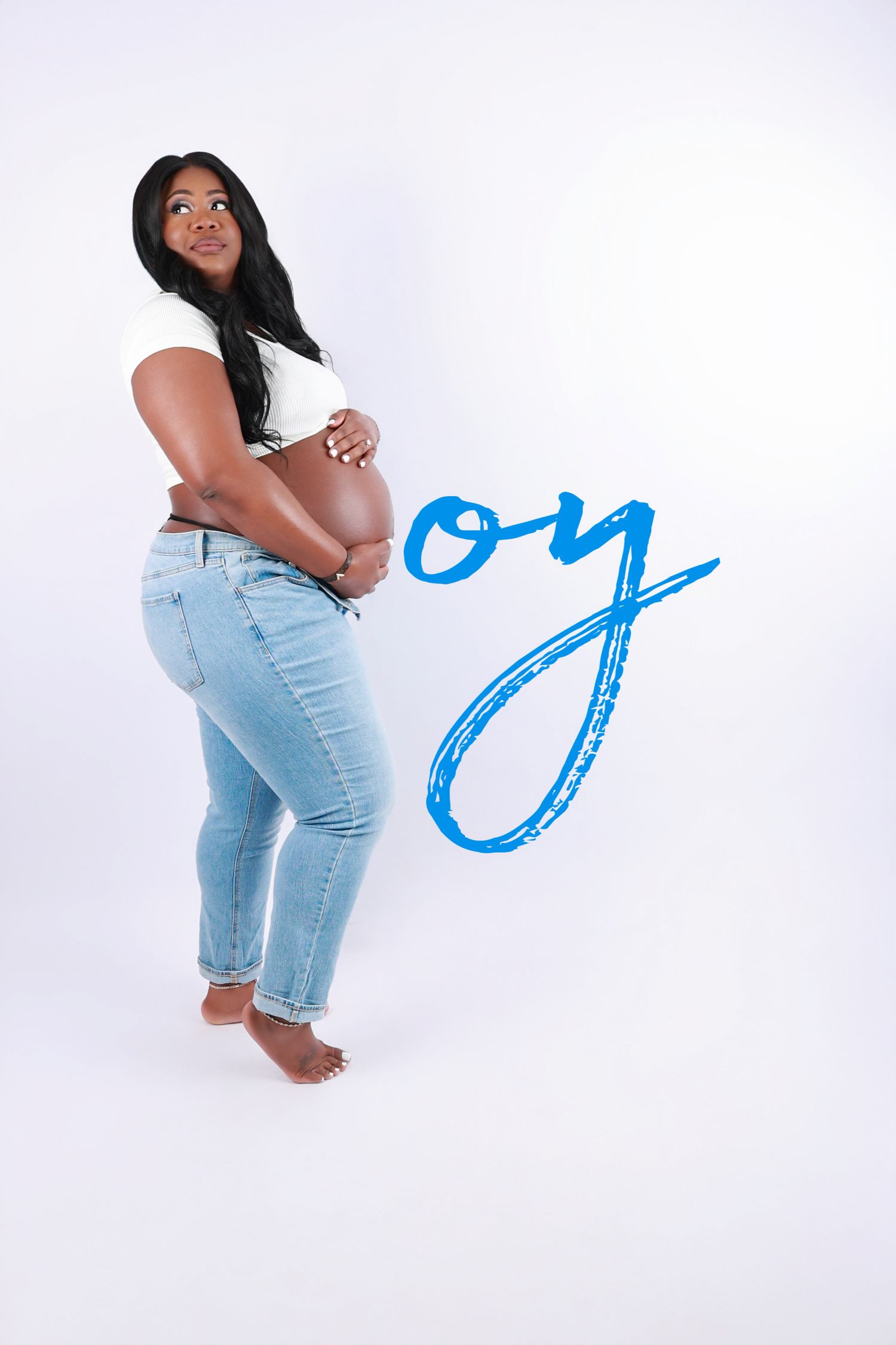 Pregnant woman in white top and jeans poses beside blue boy gender reveal text on white background.