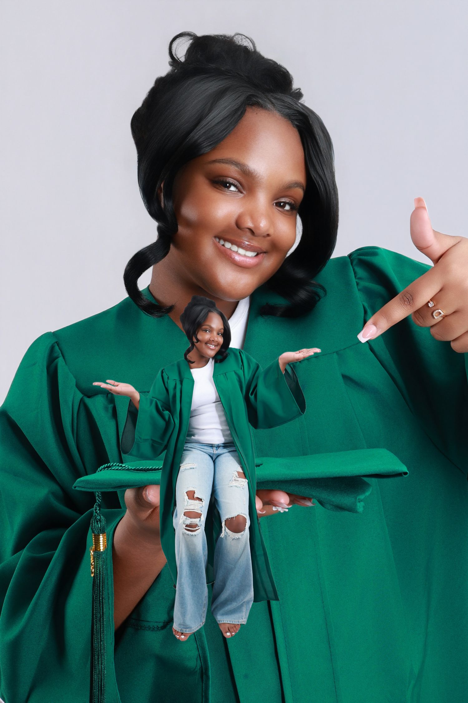A girl in a green graduation gown holds a miniature figurine of herself pointing at it.