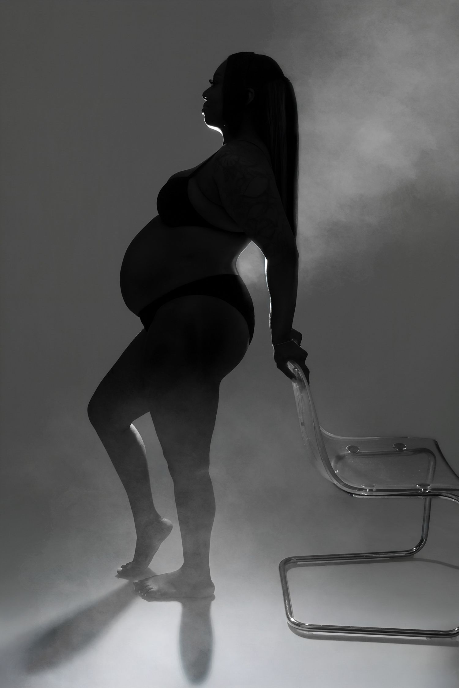 A stunning black and white silhouette of a pregnant woman posing gracefully beside a chair.