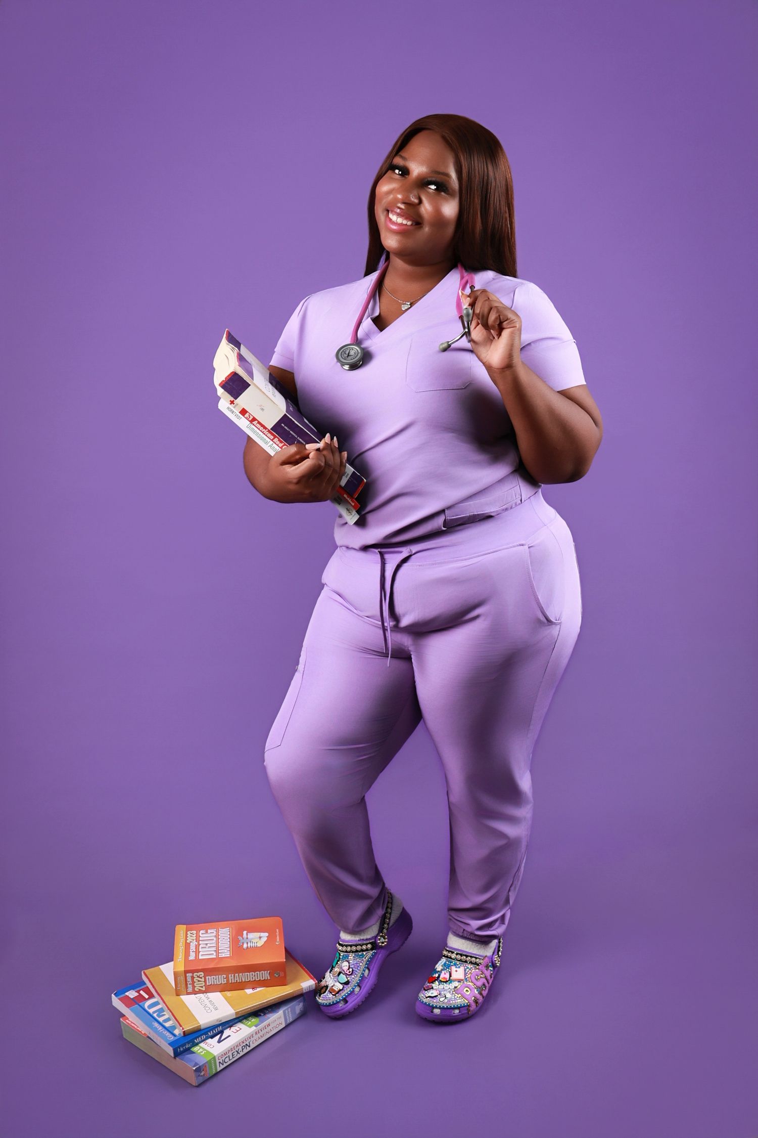 Woman in purple scrubs uniform holding medical supplies in a vibrant purple studio setting.