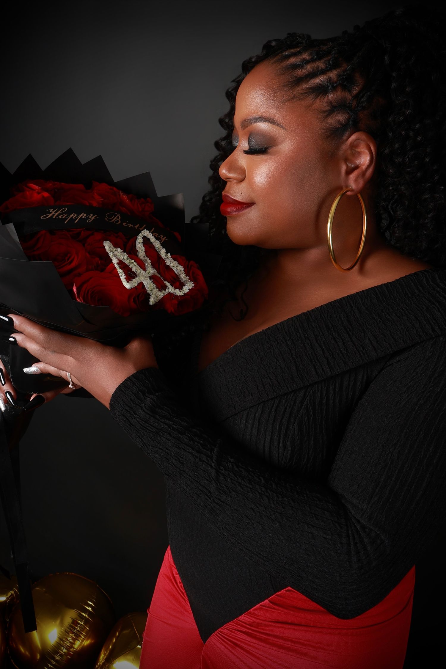 Woman celebrating 40th birthday holding bouquet of red roses with gold 40 number decoration.