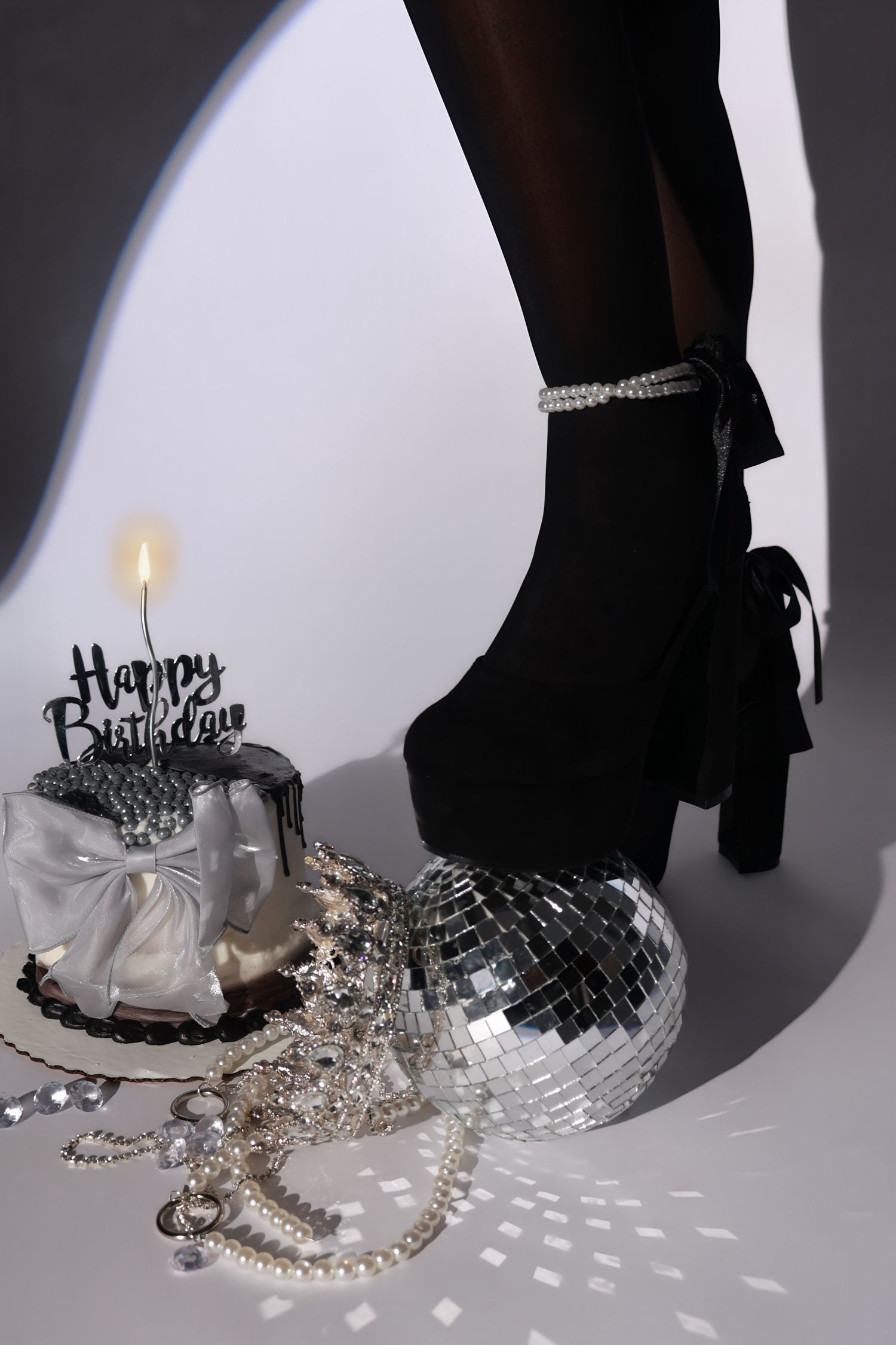 A close-up of black platform heels beside a Happy Birthday cake and disco ball accessories.