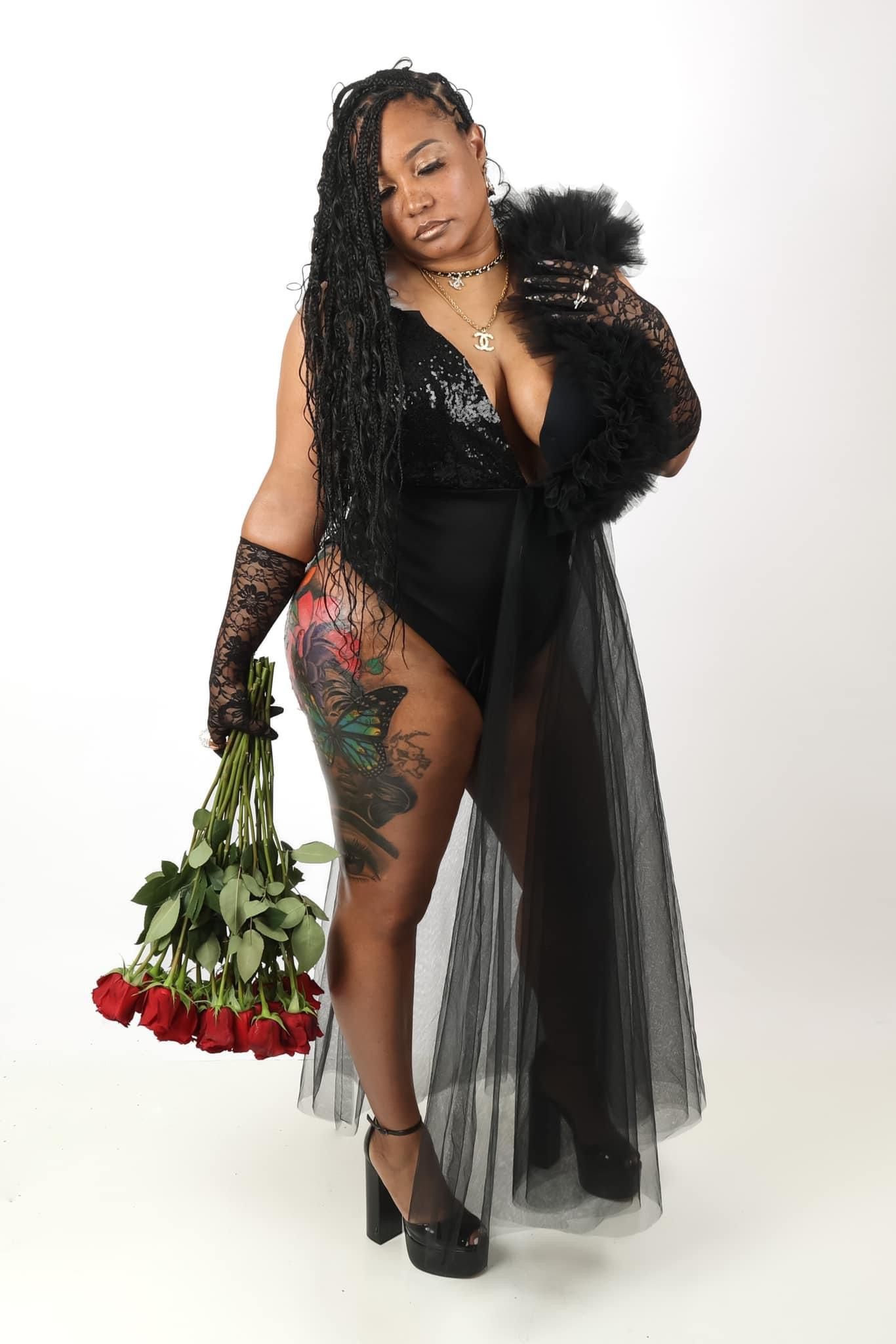 Woman in black lace robe holding red roses with tattoos visible in studio portrait.