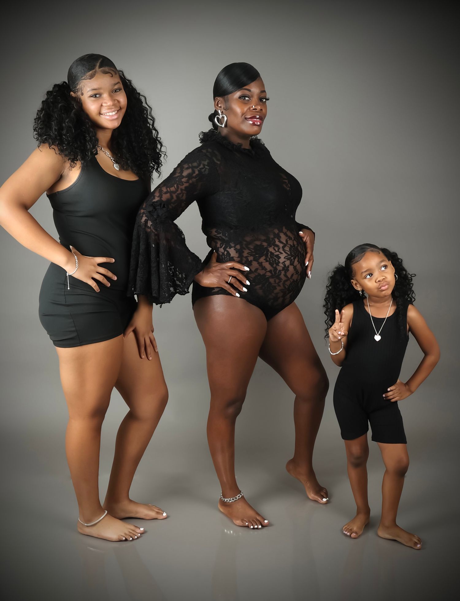 Three generations of women in matching black outfits posing together in studio portrait.