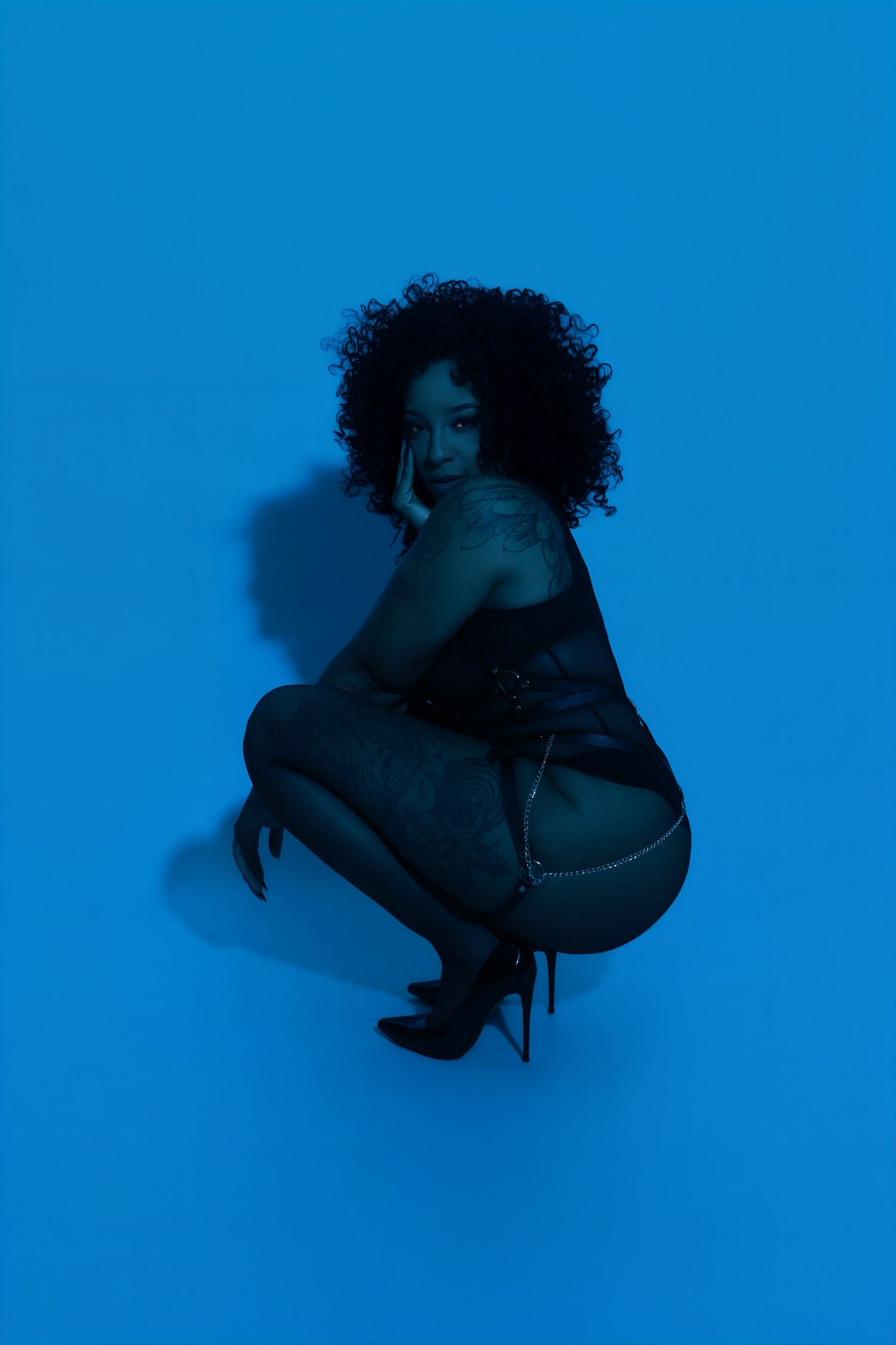 Woman with curly hair  in black outfit under blue studio lighting.