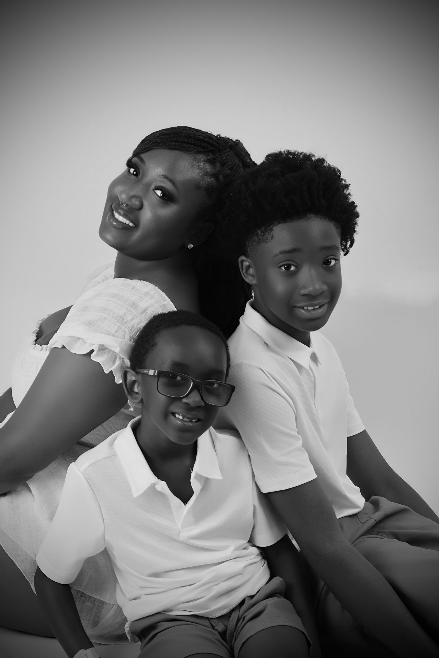 Black and white studio portrait of a woman and two children sitting back to back smiling.