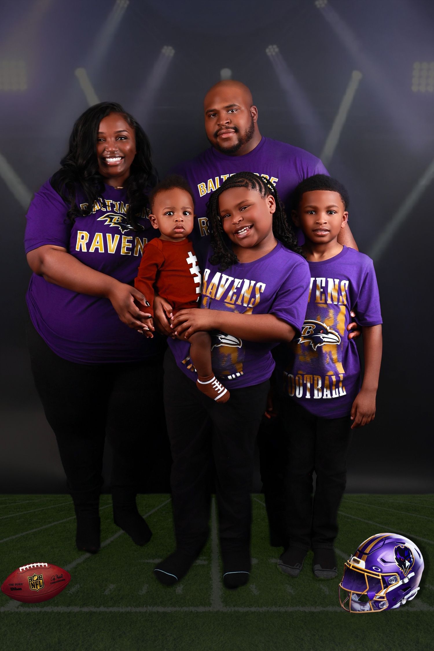 Family of five wearing Baltimore Ravens purple jerseys posing on football field backdrop.