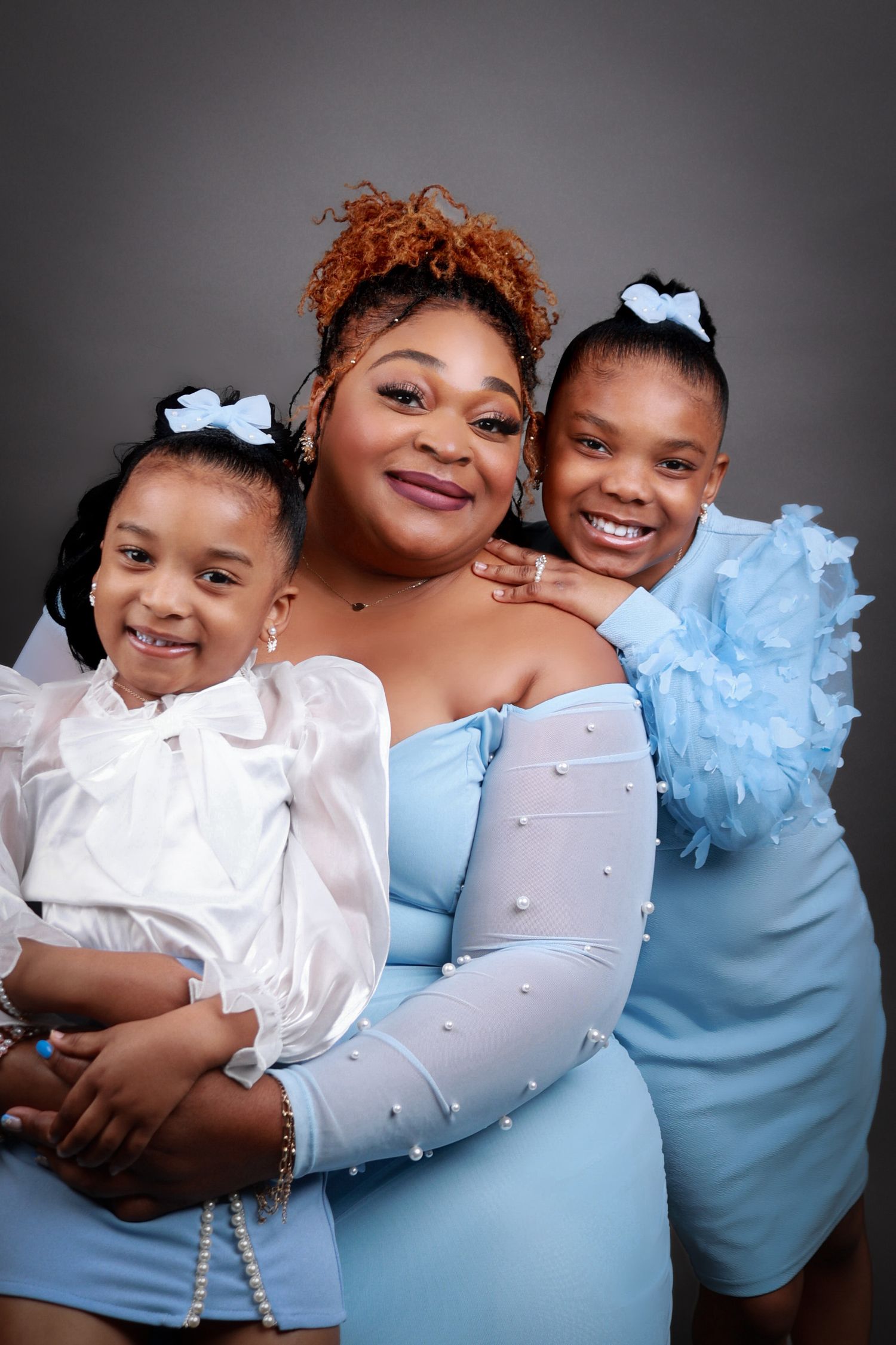 Mother and two daughters smiling together in coordinating blue and white outfits in studio.