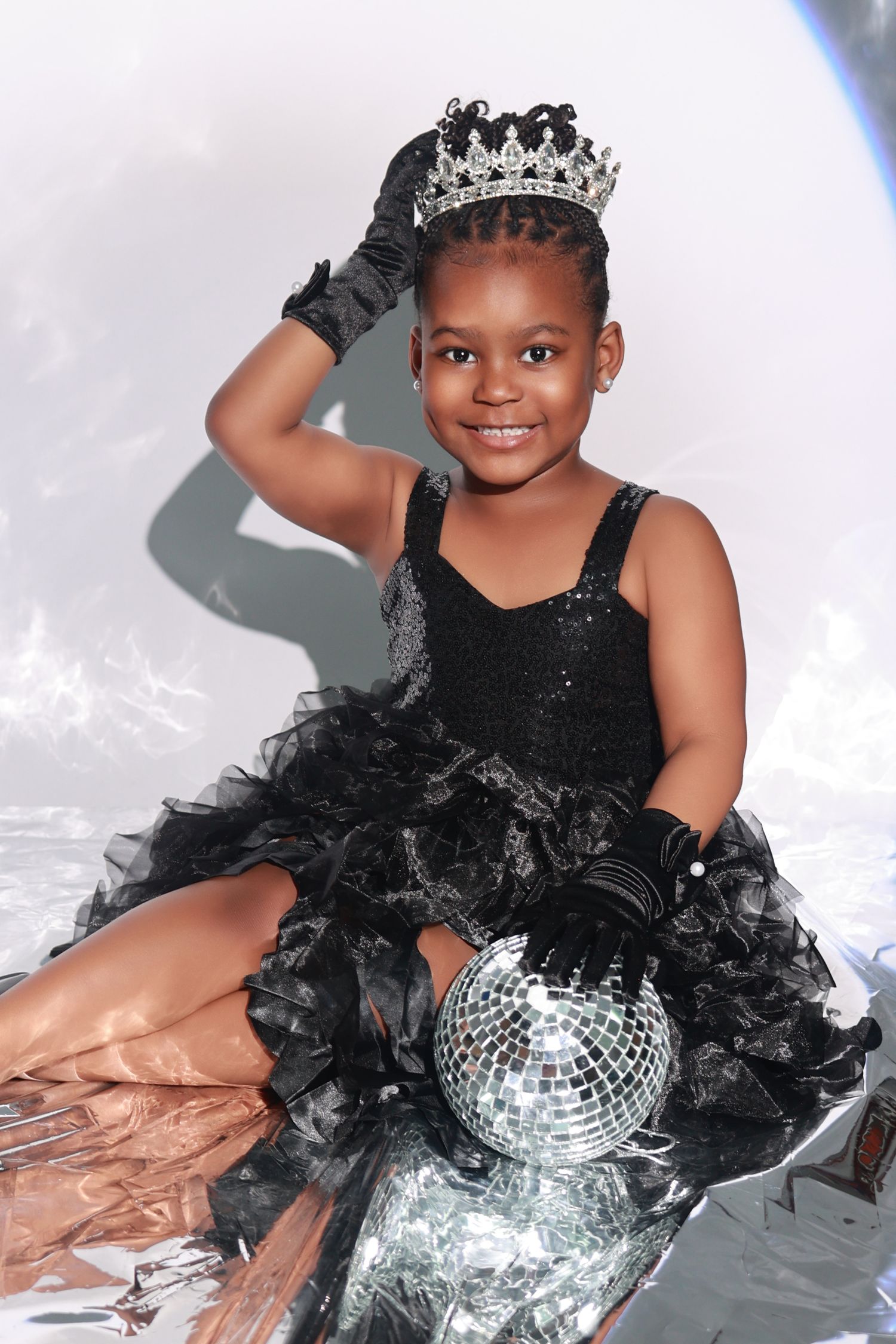 Young girl in black dress wearing crown holding disco ball in studio portrait.